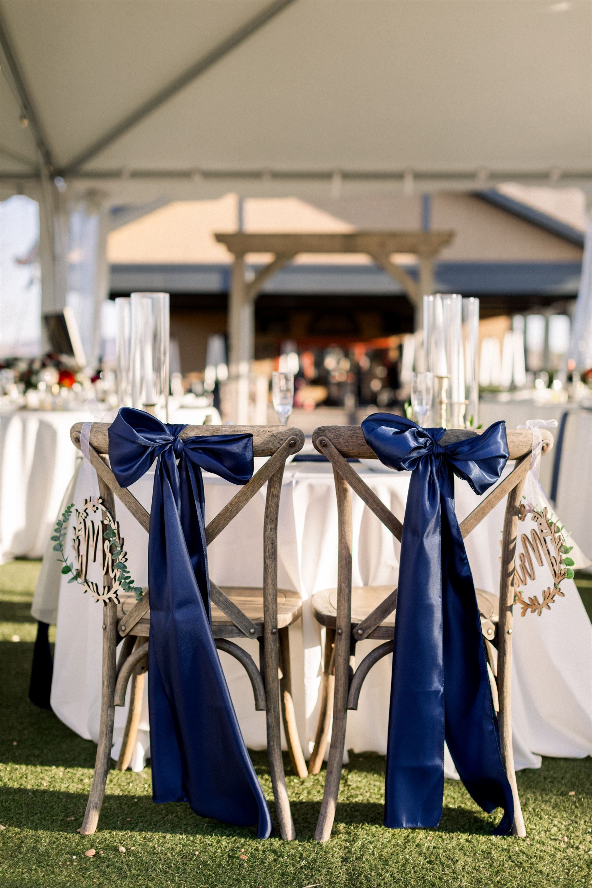 Two wooden chairs with navy bows at a wedding reception table.