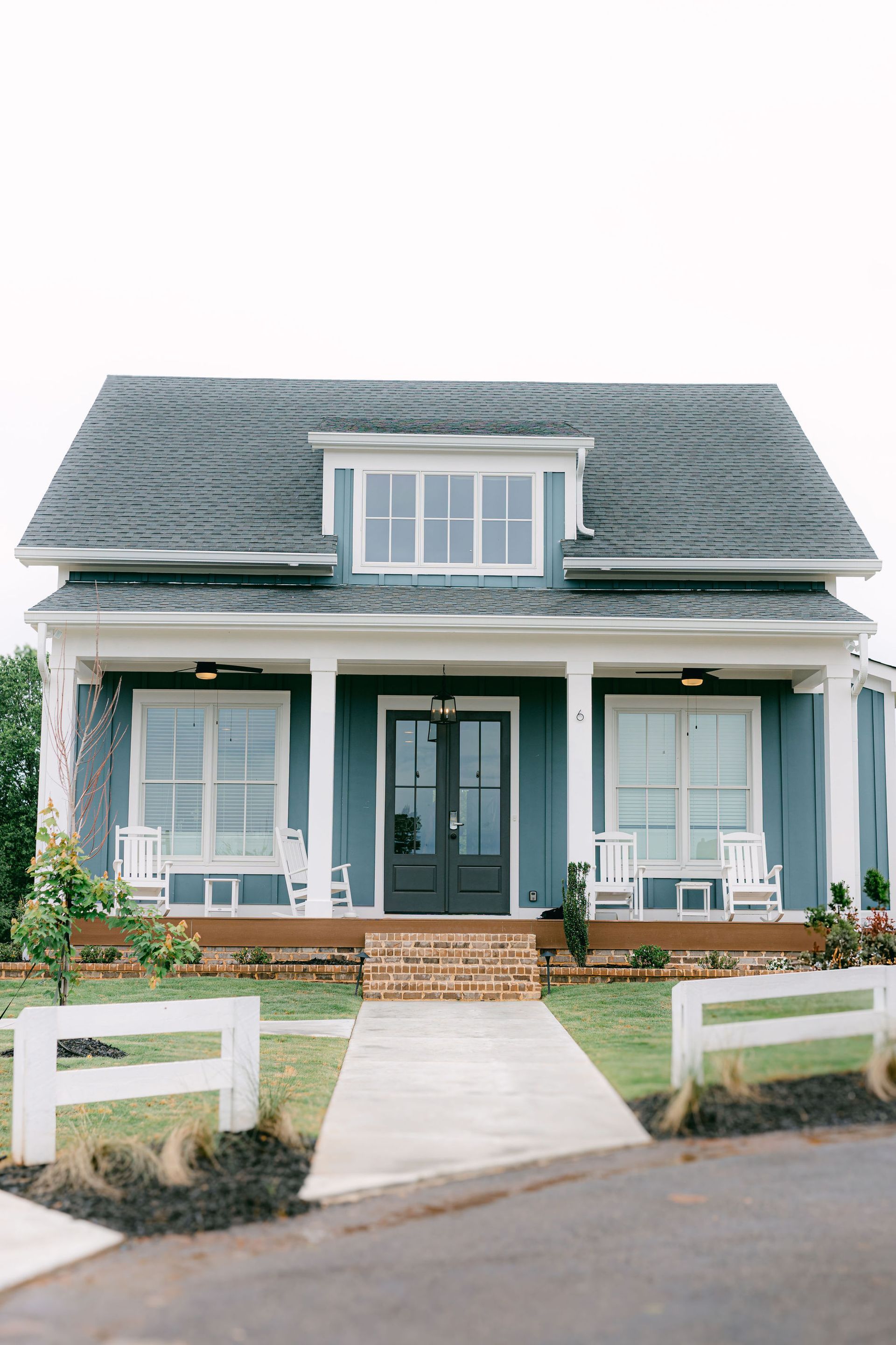 Blue house with white trim, porch, and a brick pathway leading to the front door.
