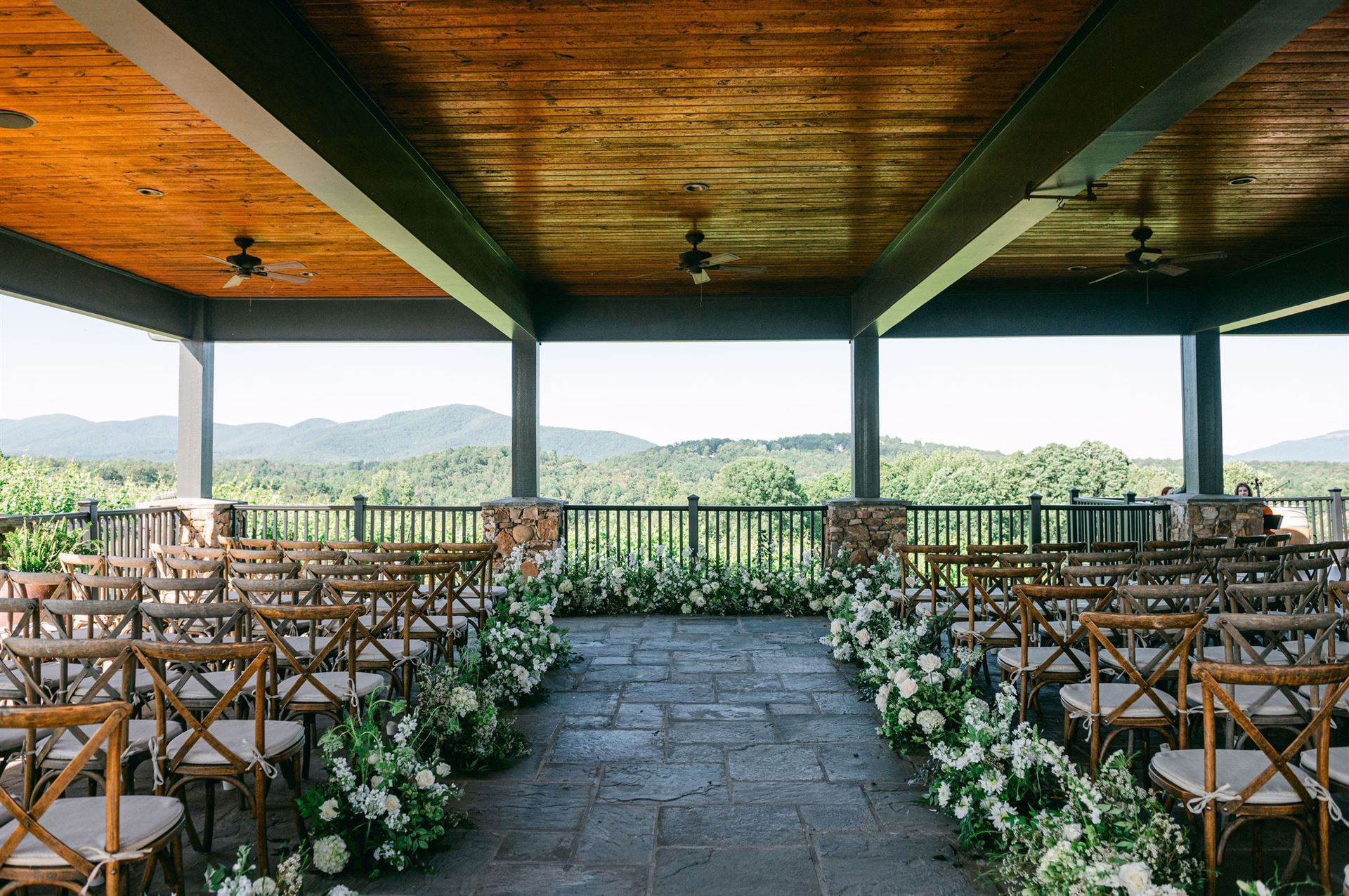 Wedding ceremony setup: chairs, floral arrangements, mountain view from covered outdoor pavilion.
