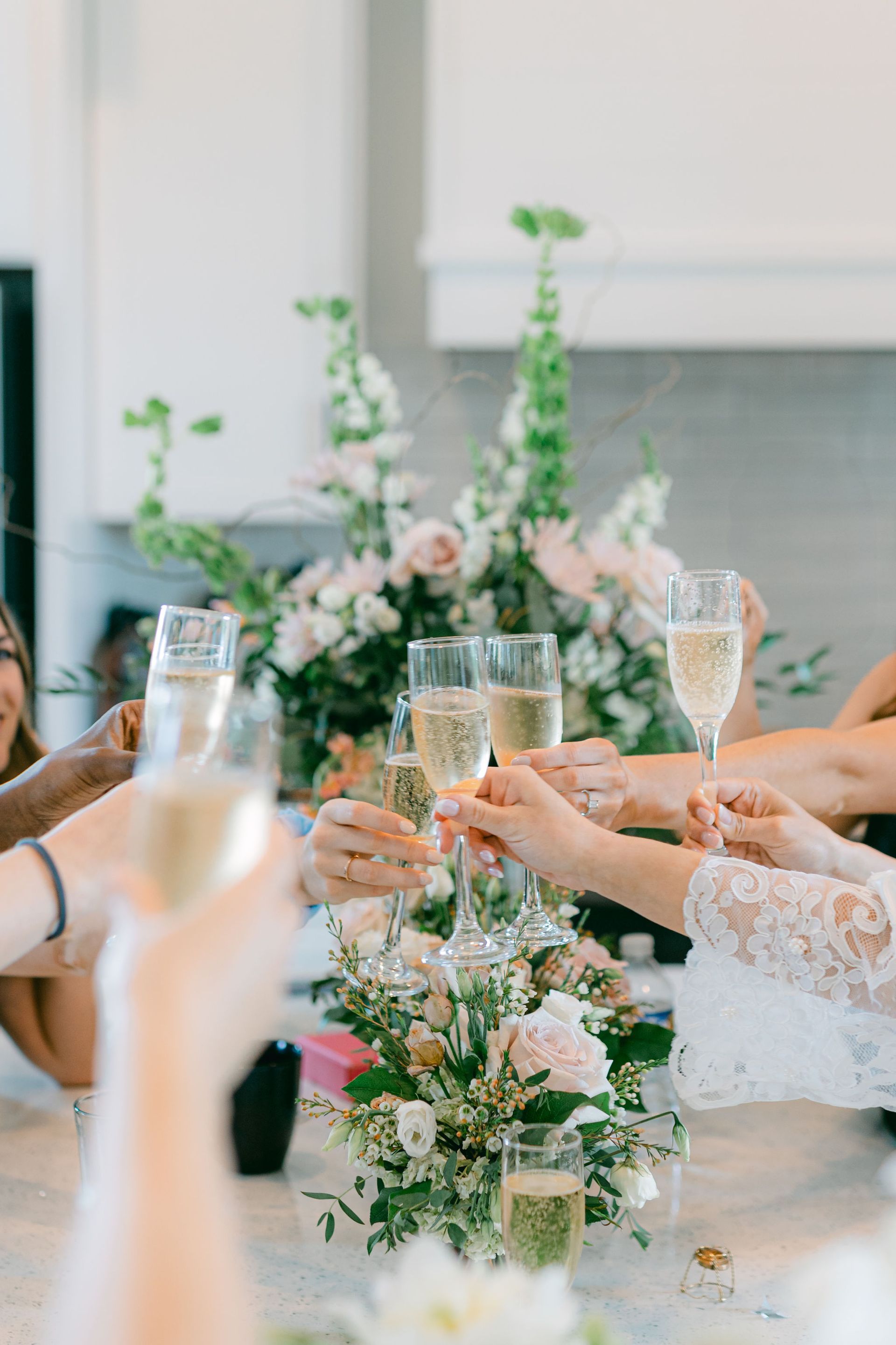 People toasting champagne glasses with floral arrangement.