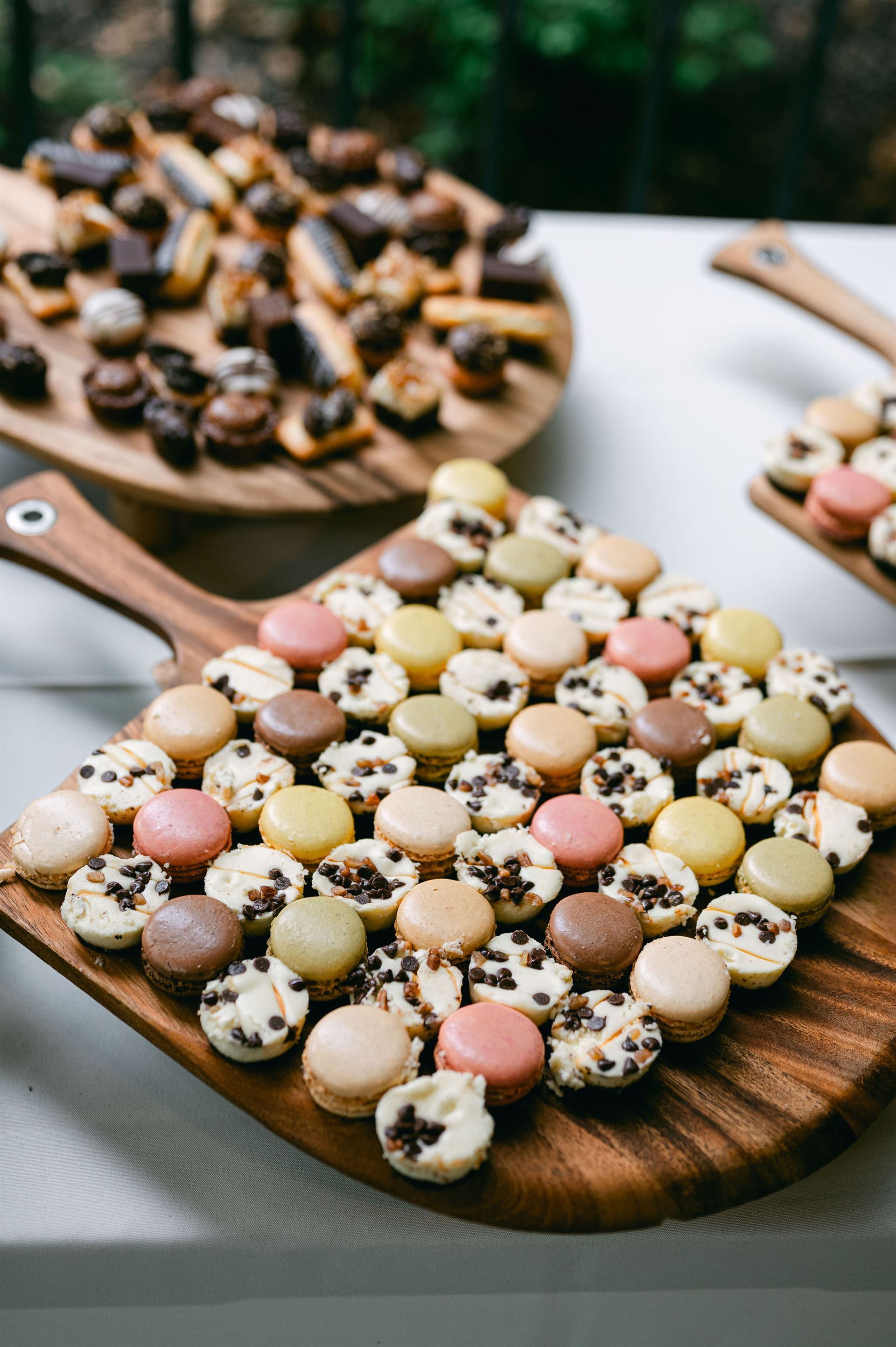 Wooden platters of colorful macarons and other pastries on a white tablecloth.