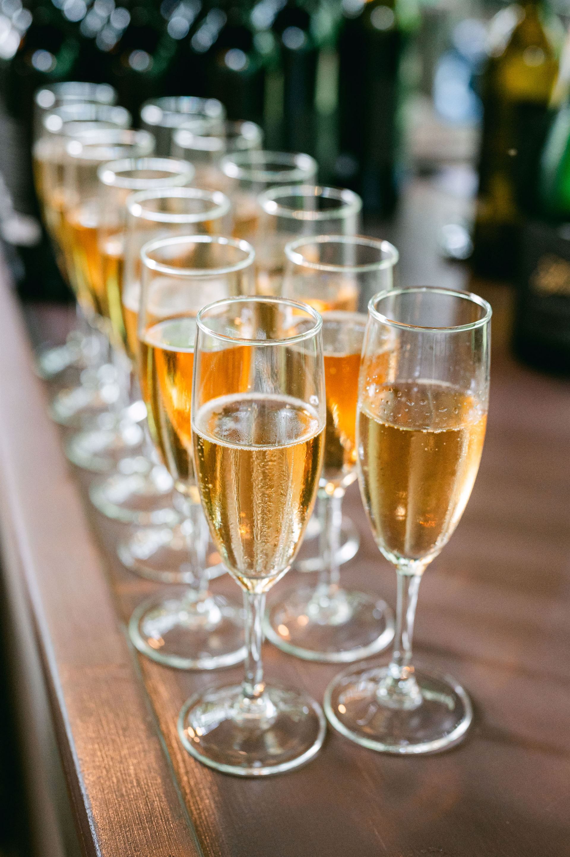 Rows of champagne flutes filled with bubbly, golden liquid on a brown surface.