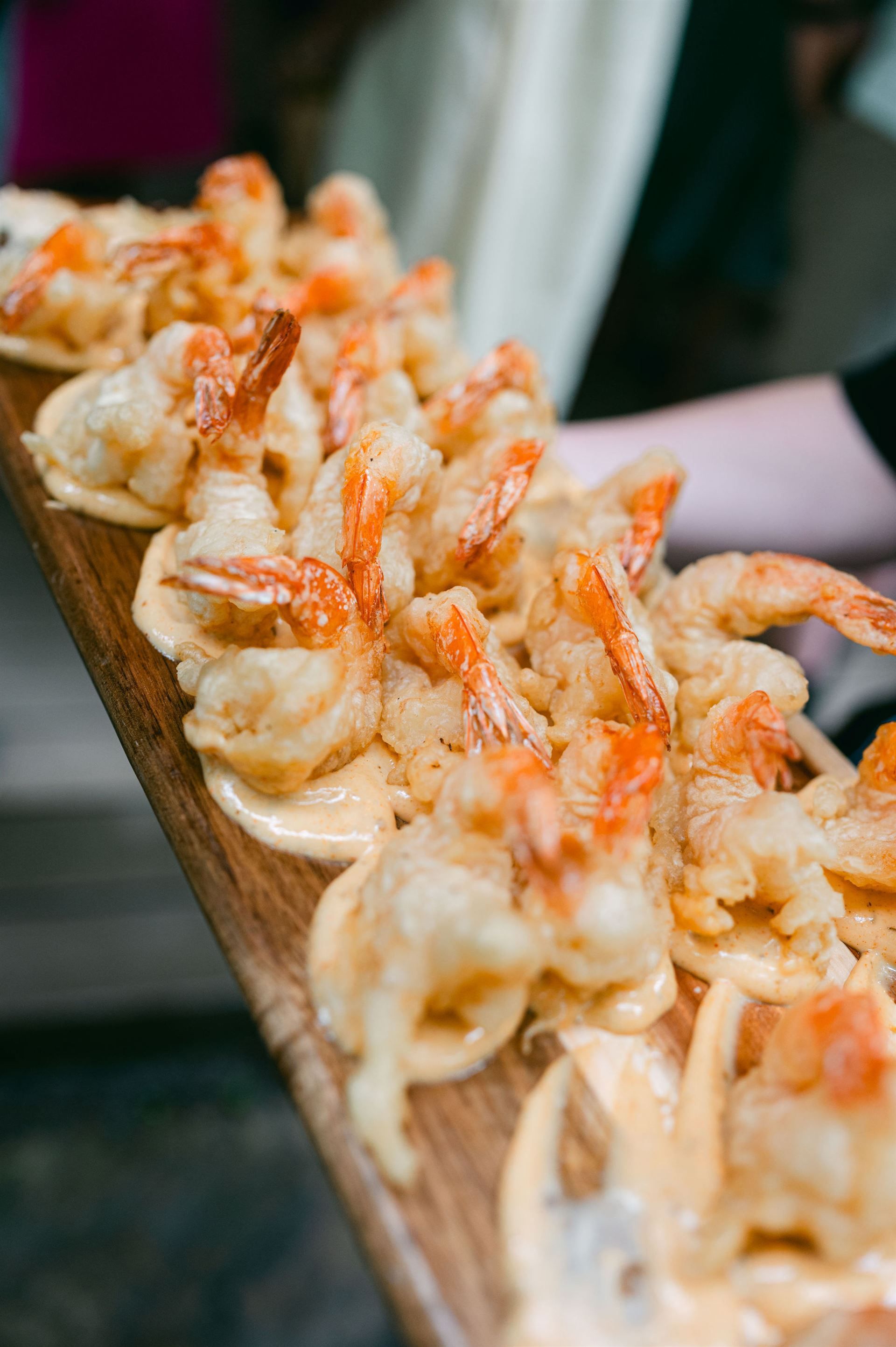 Fried shrimp on a wooden serving board, topped with sauce.