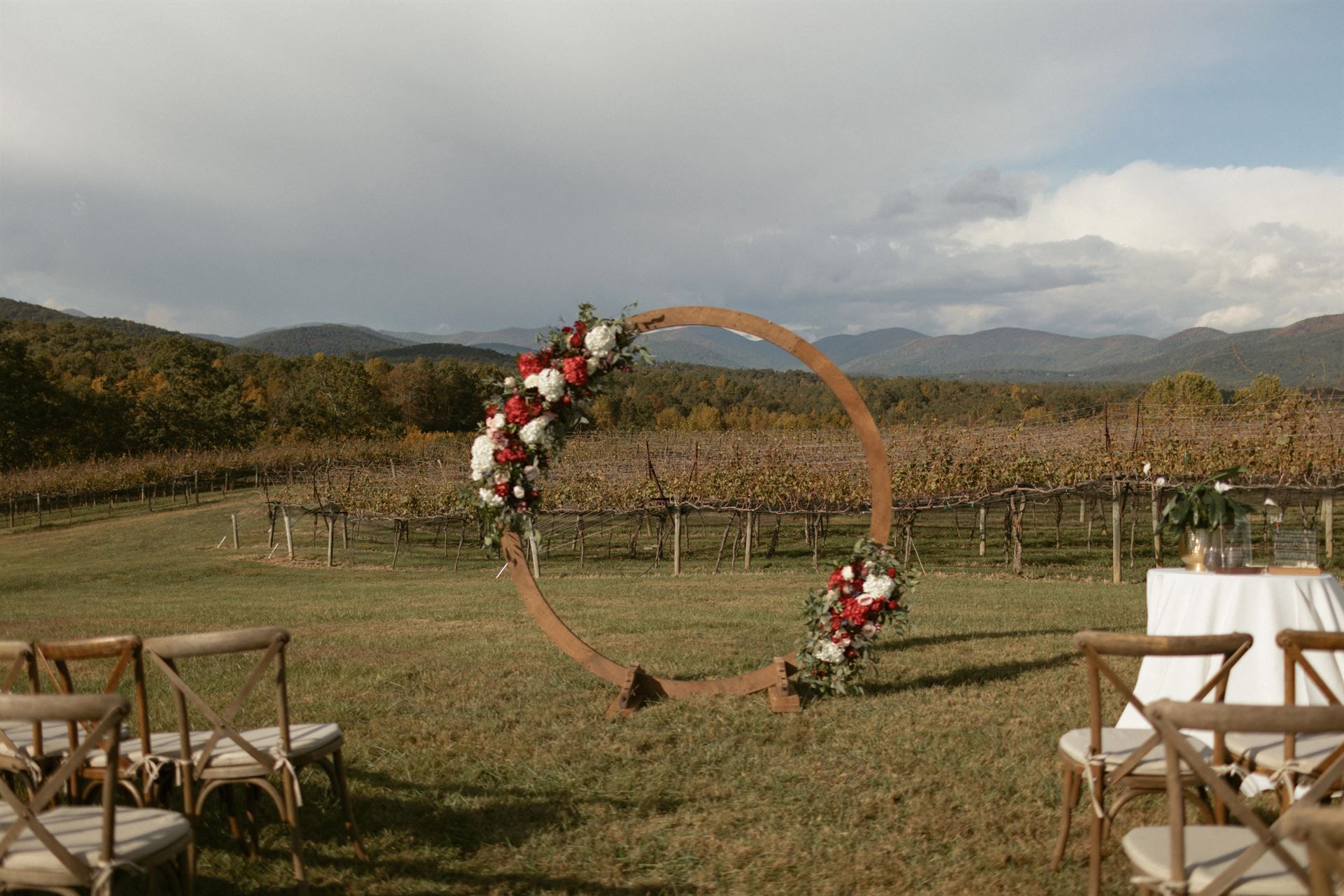 Wedding ceremony setup with floral arch overlooking vineyard and mountains.