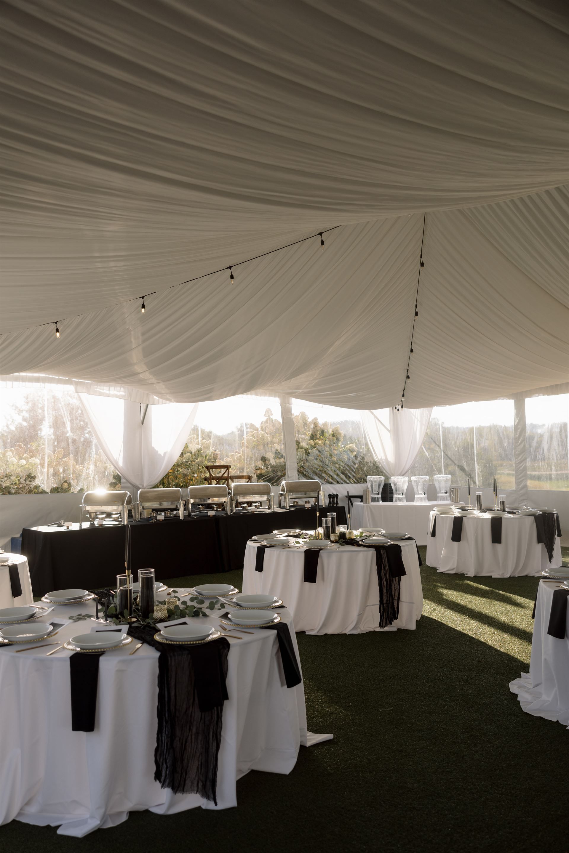 Wedding reception tables with white tablecloths and black accents, under a white tent.