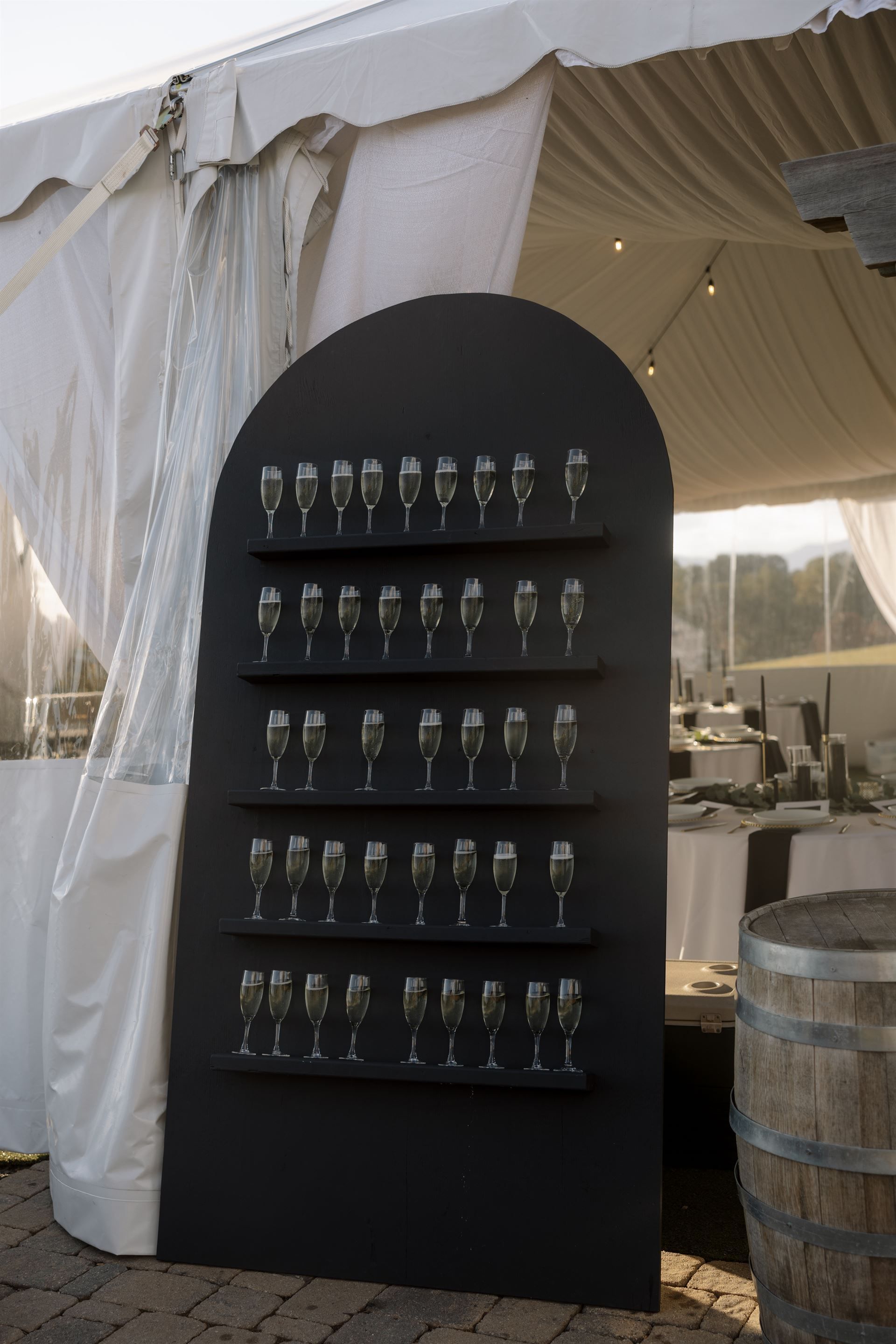 Black champagne glass display with glasses, under a white tent at an outdoor event.