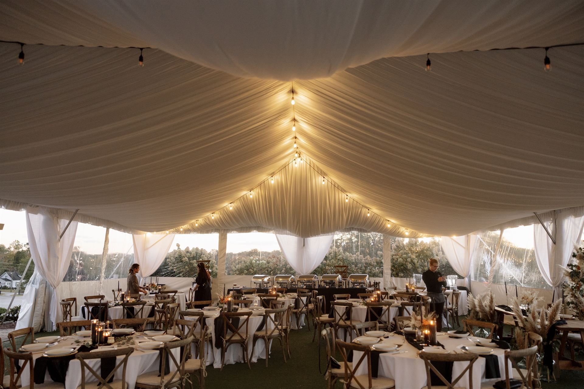Wedding reception tent decorated with string lights, tables, and chairs.