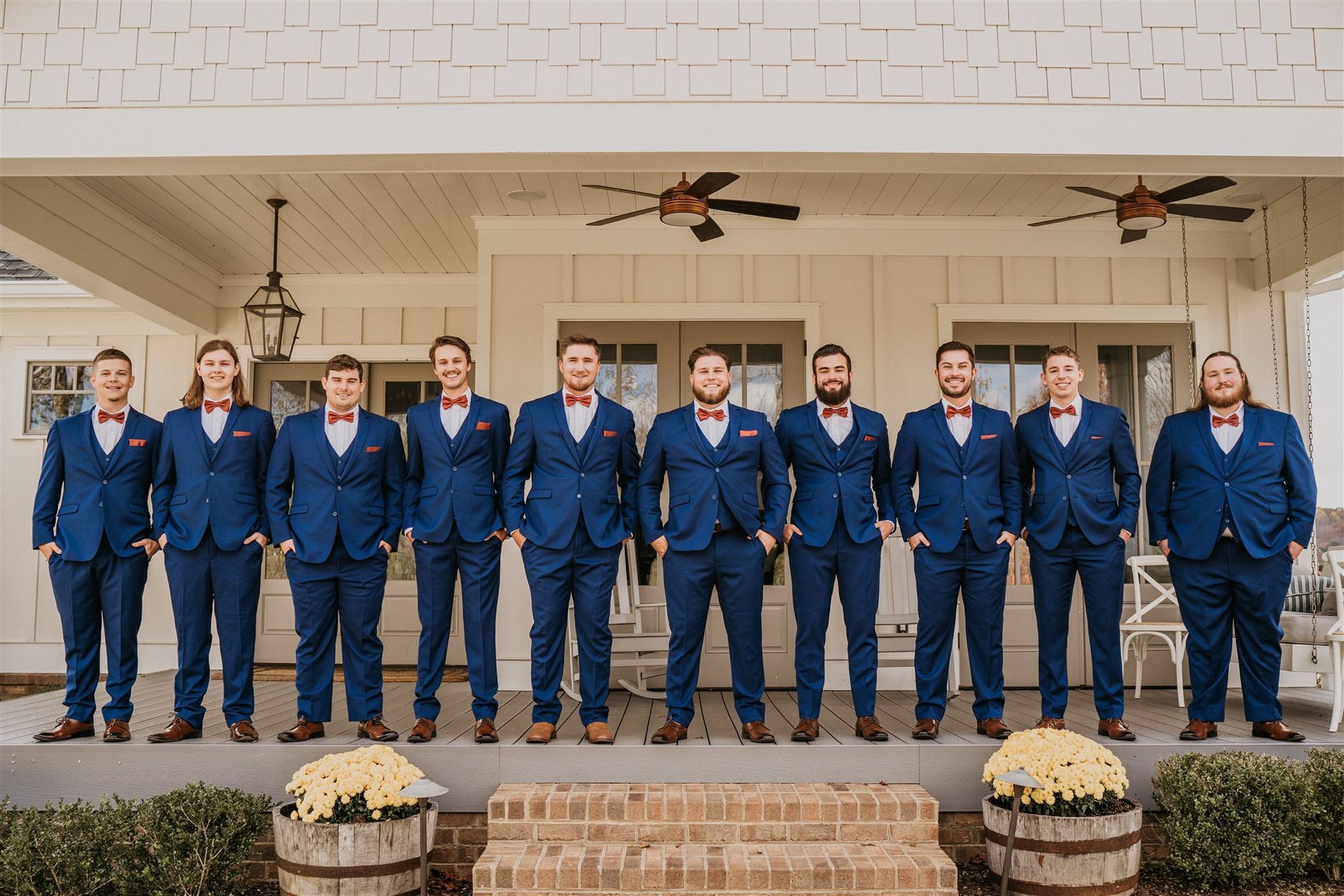 Group of men in blue suits and red bow ties pose on a porch.