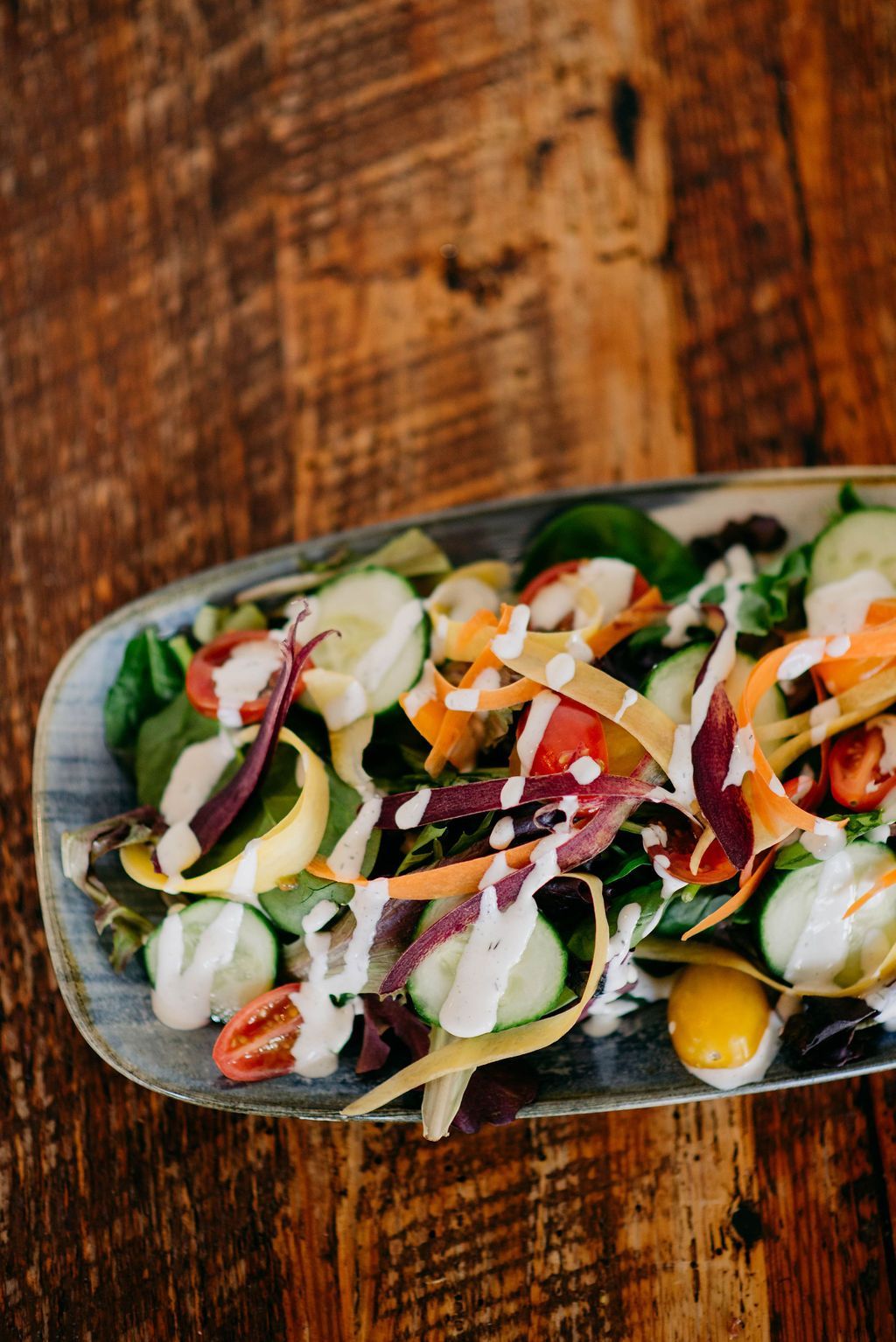Salad with cucumbers, carrots, and dressing on a blue plate, against a wooden table.
