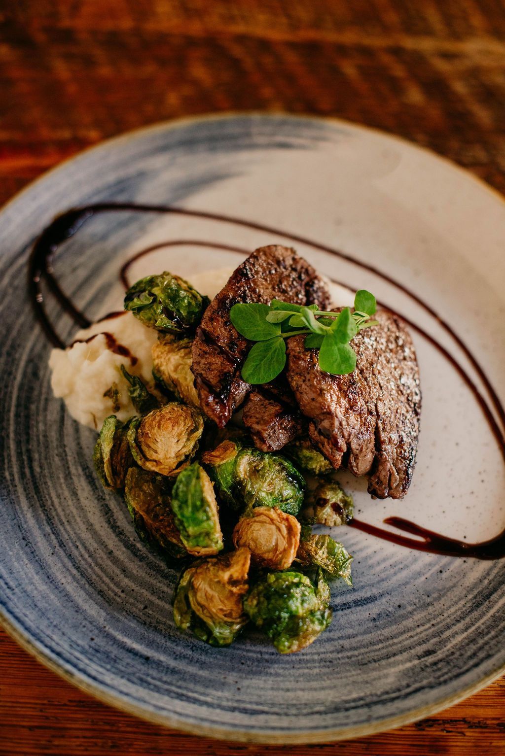 Steak with roasted Brussels sprouts and mashed potatoes on a plate with balsamic glaze.