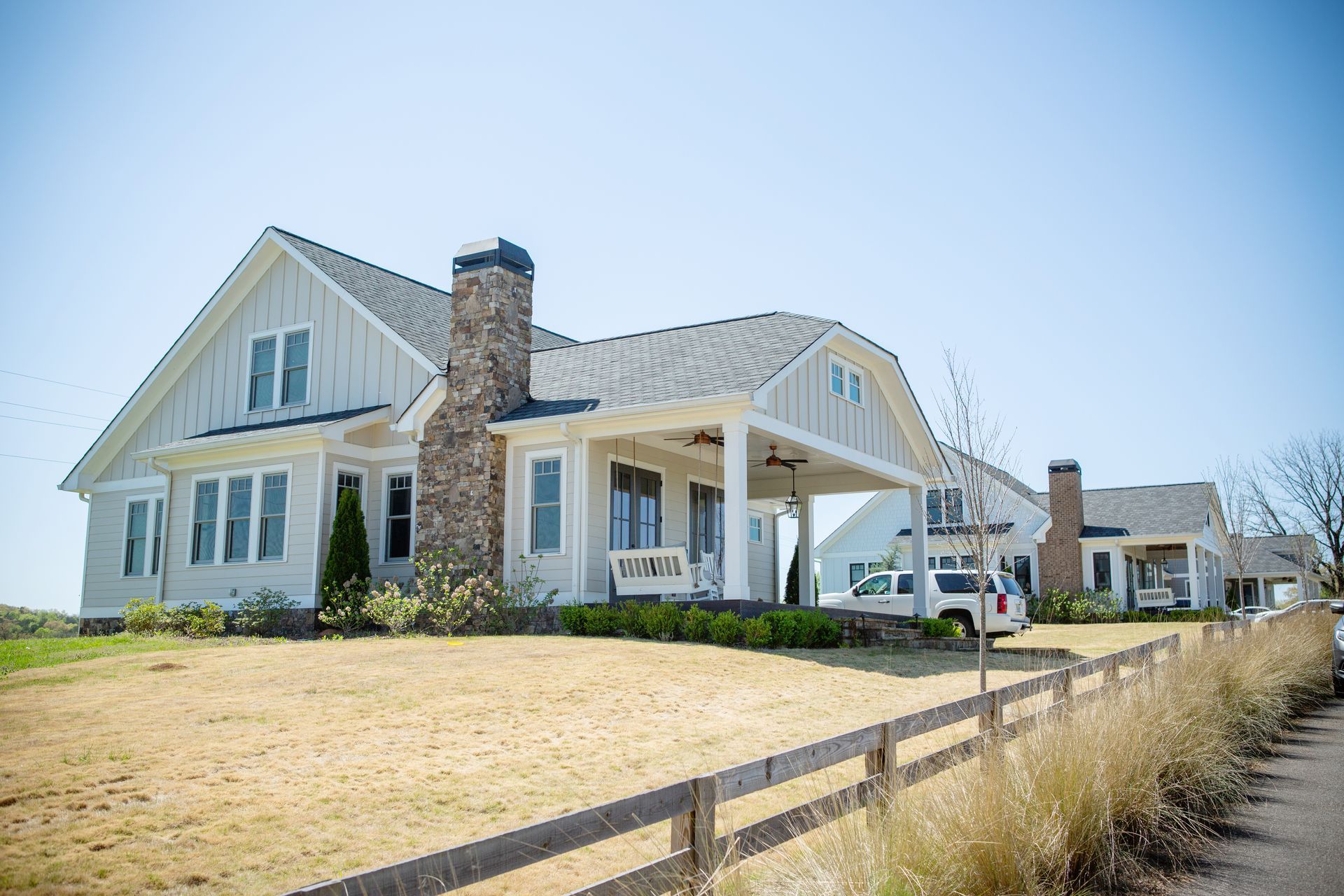 White farmhouse with a stone chimney, covered porch, and brown fence on a sunny day.