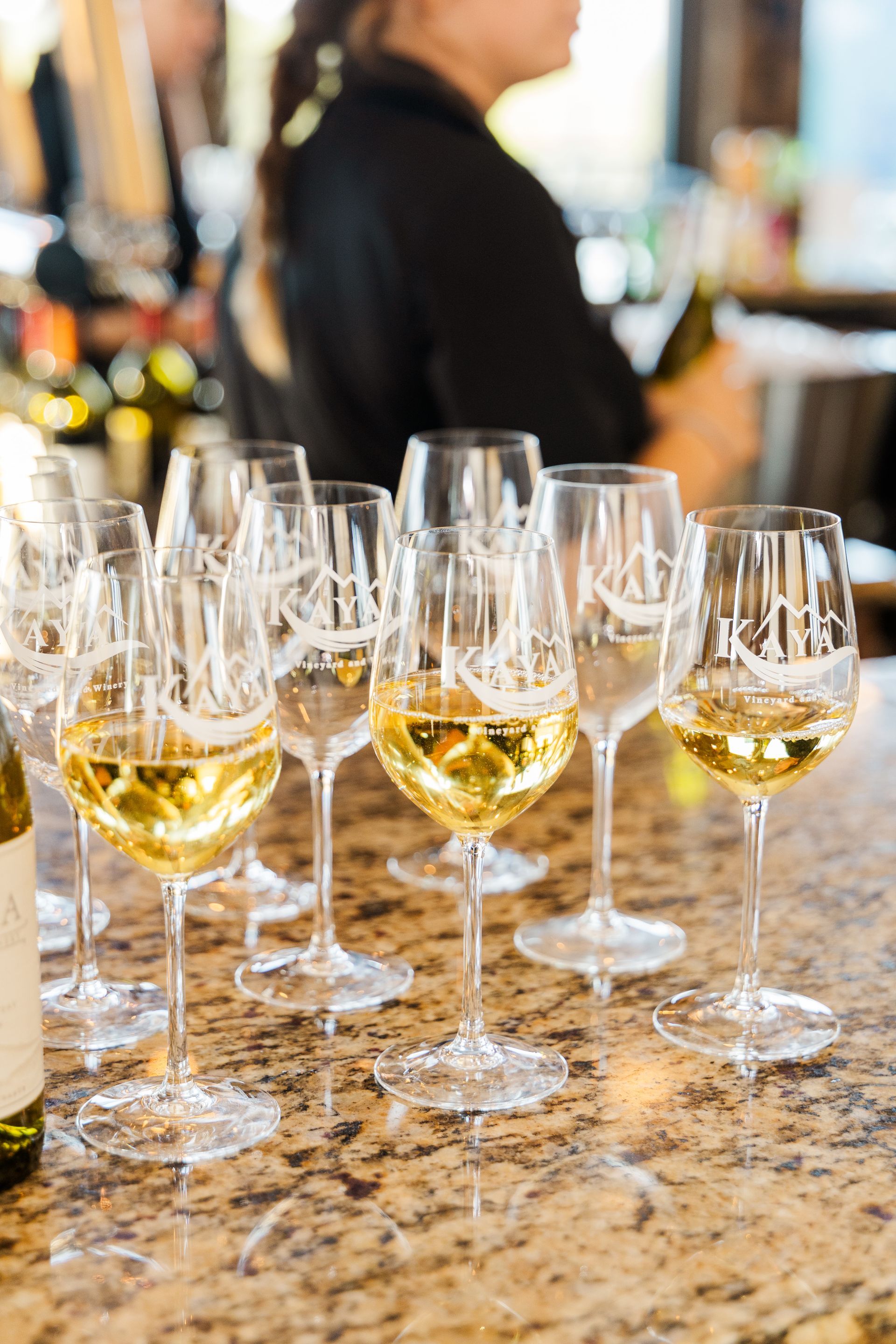 Wine glasses filled with white wine on a counter. A person in the background.