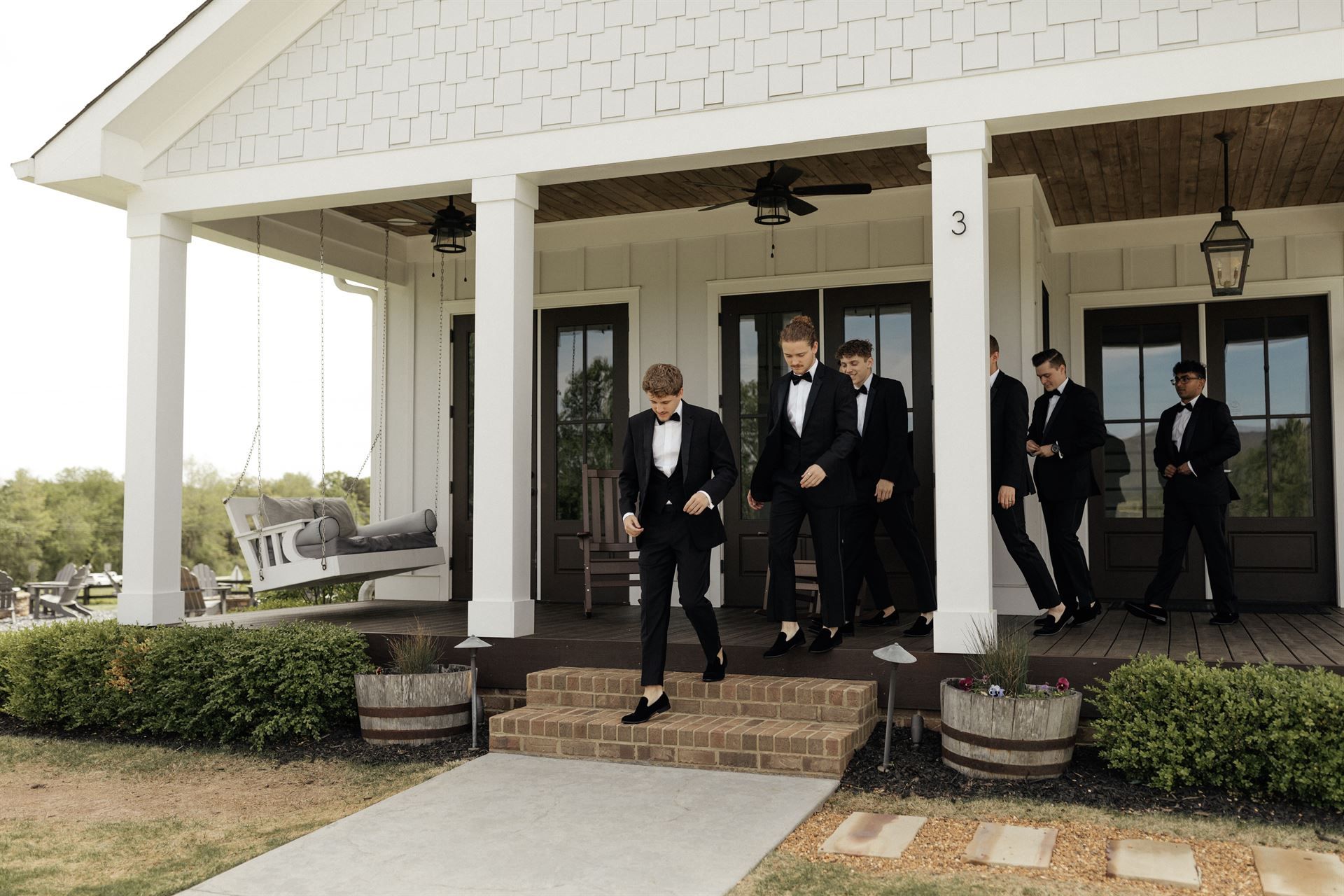 Men in tuxedos exiting a white porch, preparing for a wedding.