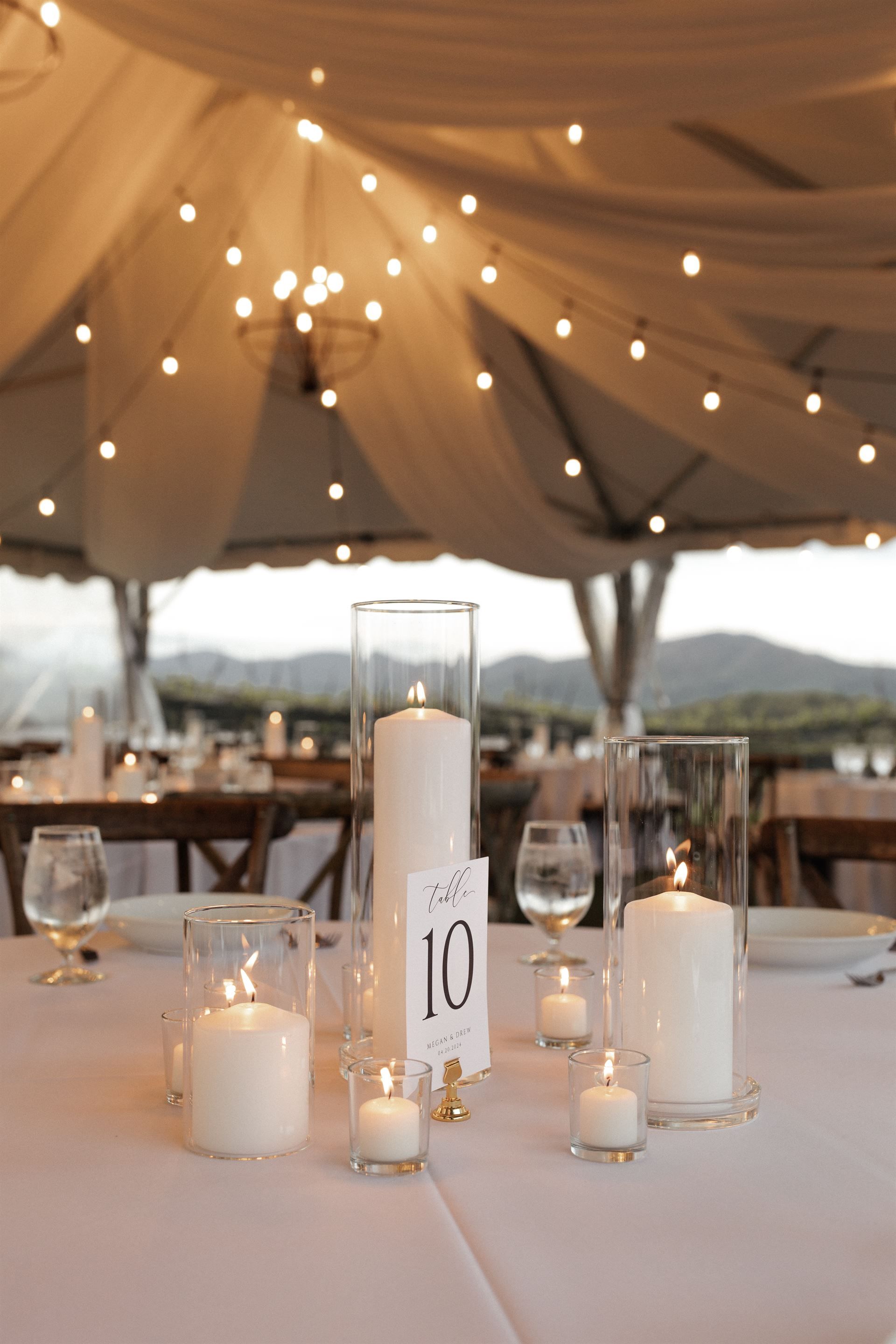 Wedding reception table with candles and string lights under a tent. Table number 10.