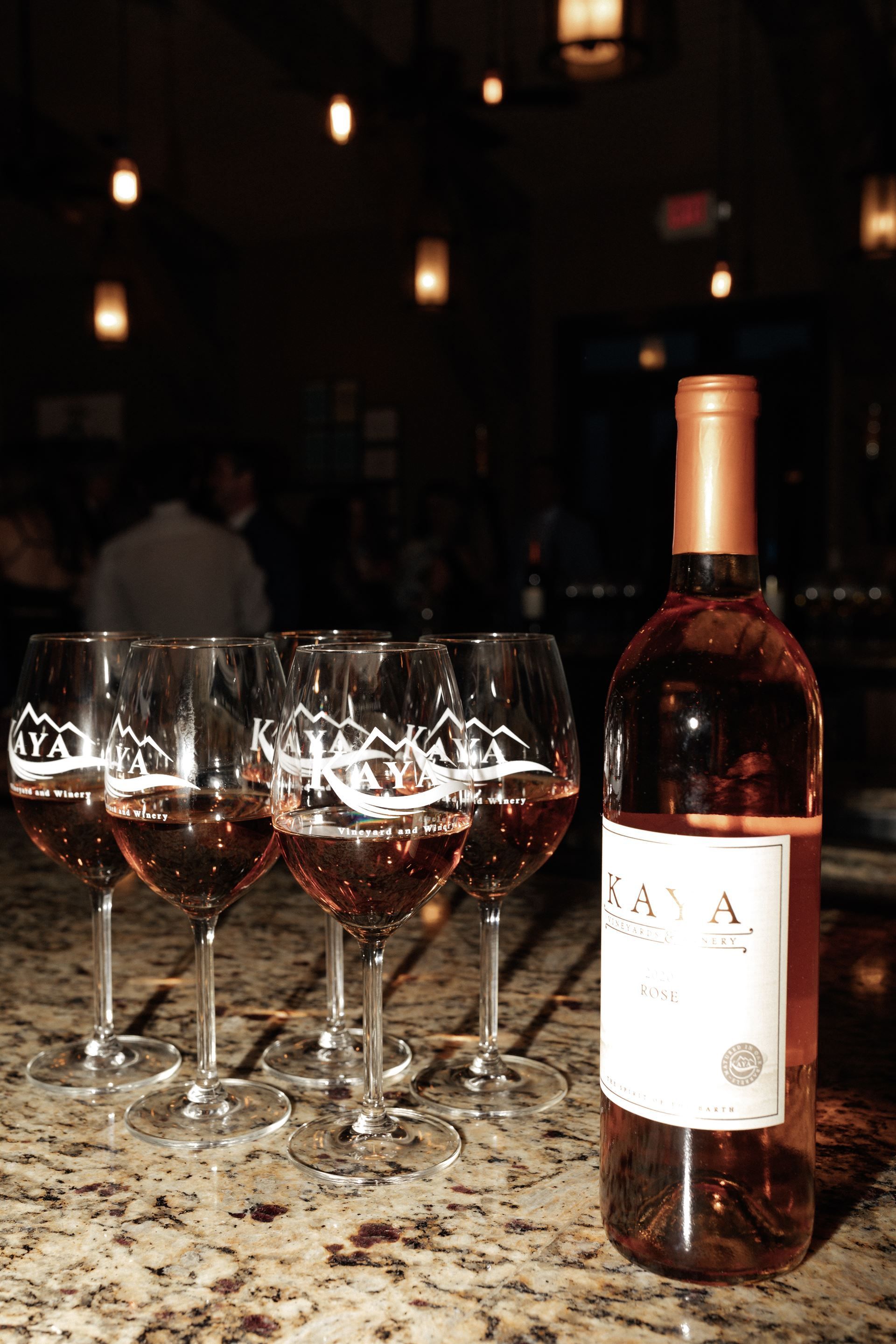 A bottle of rosé wine and four filled wine glasses sit on a bar.