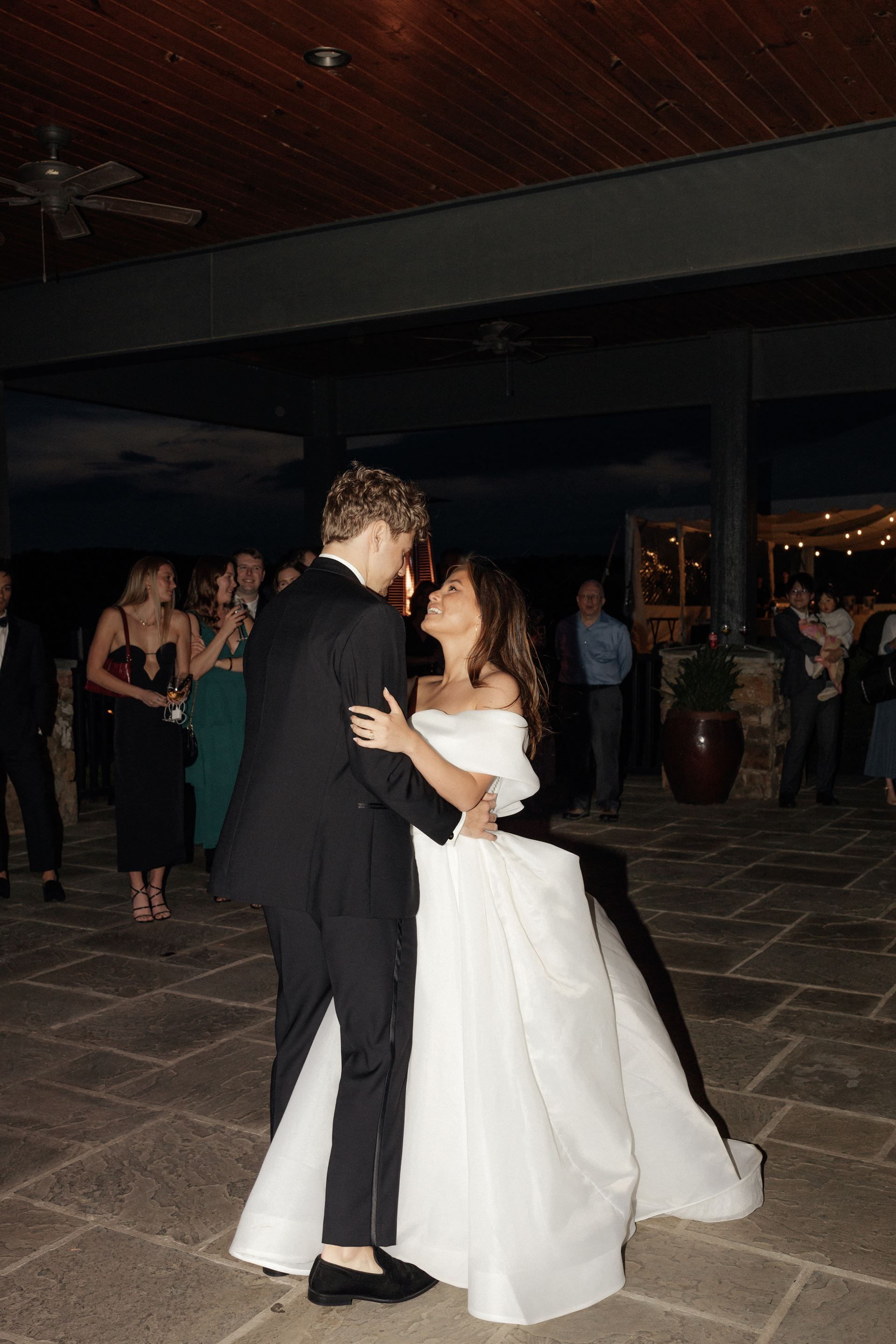 Couple dancing at a wedding reception. Woman in a white gown, man in a black suit, looking at each other.