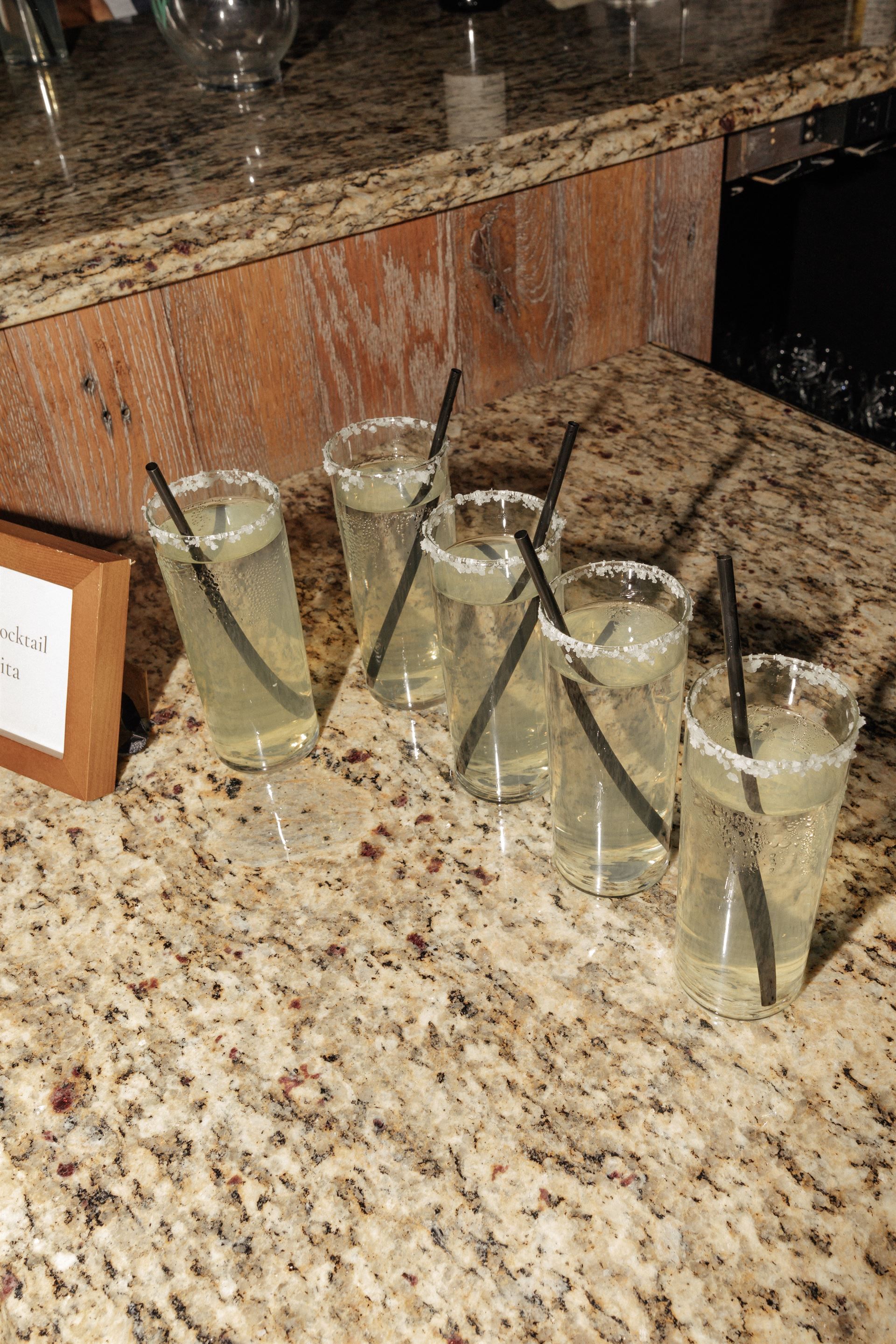 Cocktails on a granite countertop, in clear glasses with salt rims and straws.