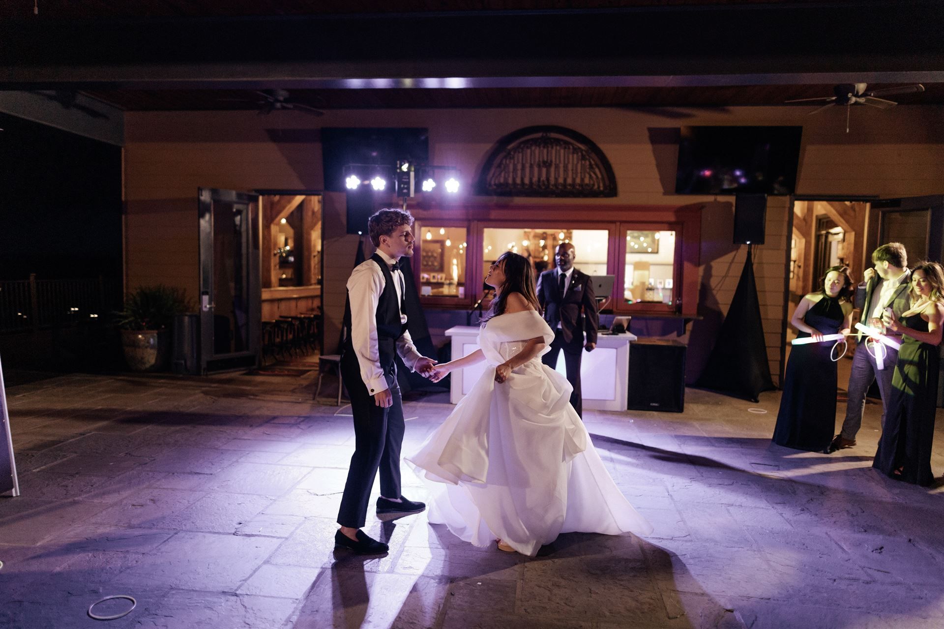 Bride and groom dancing at a wedding reception outdoors at night, with guests holding sparklers.