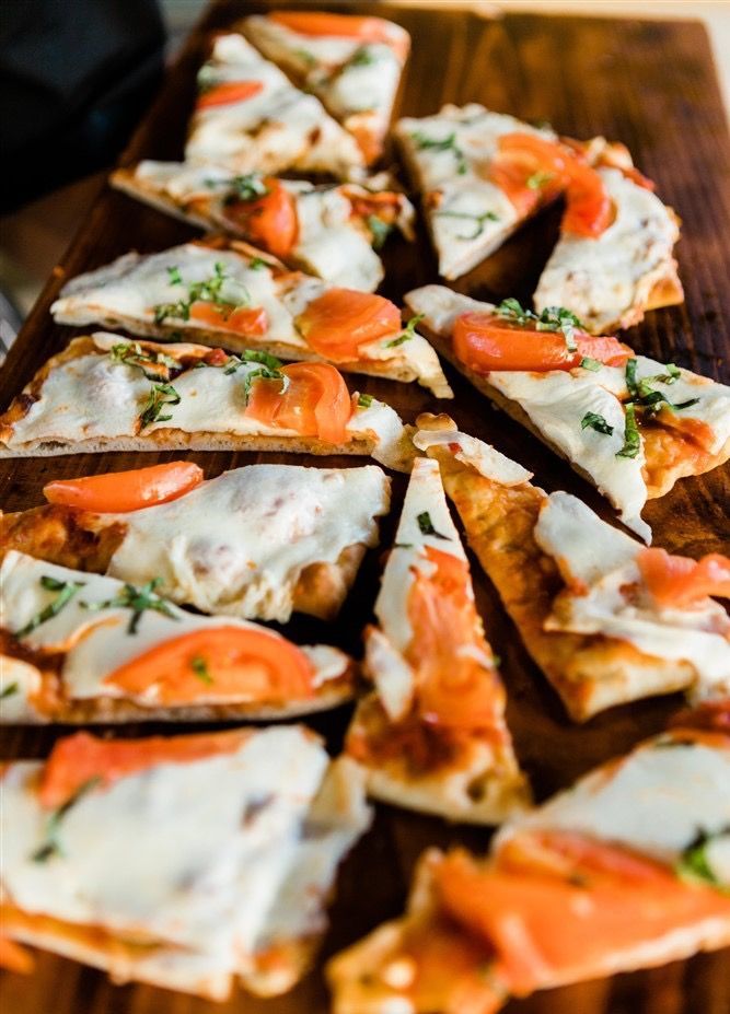 Pizza slices with cheese, tomato, and herbs on a wooden board.