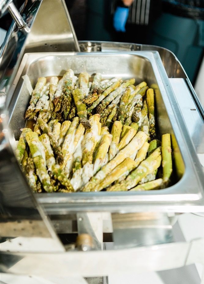 Asparagus spears coated in flour in a stainless steel food warmer at a buffet.