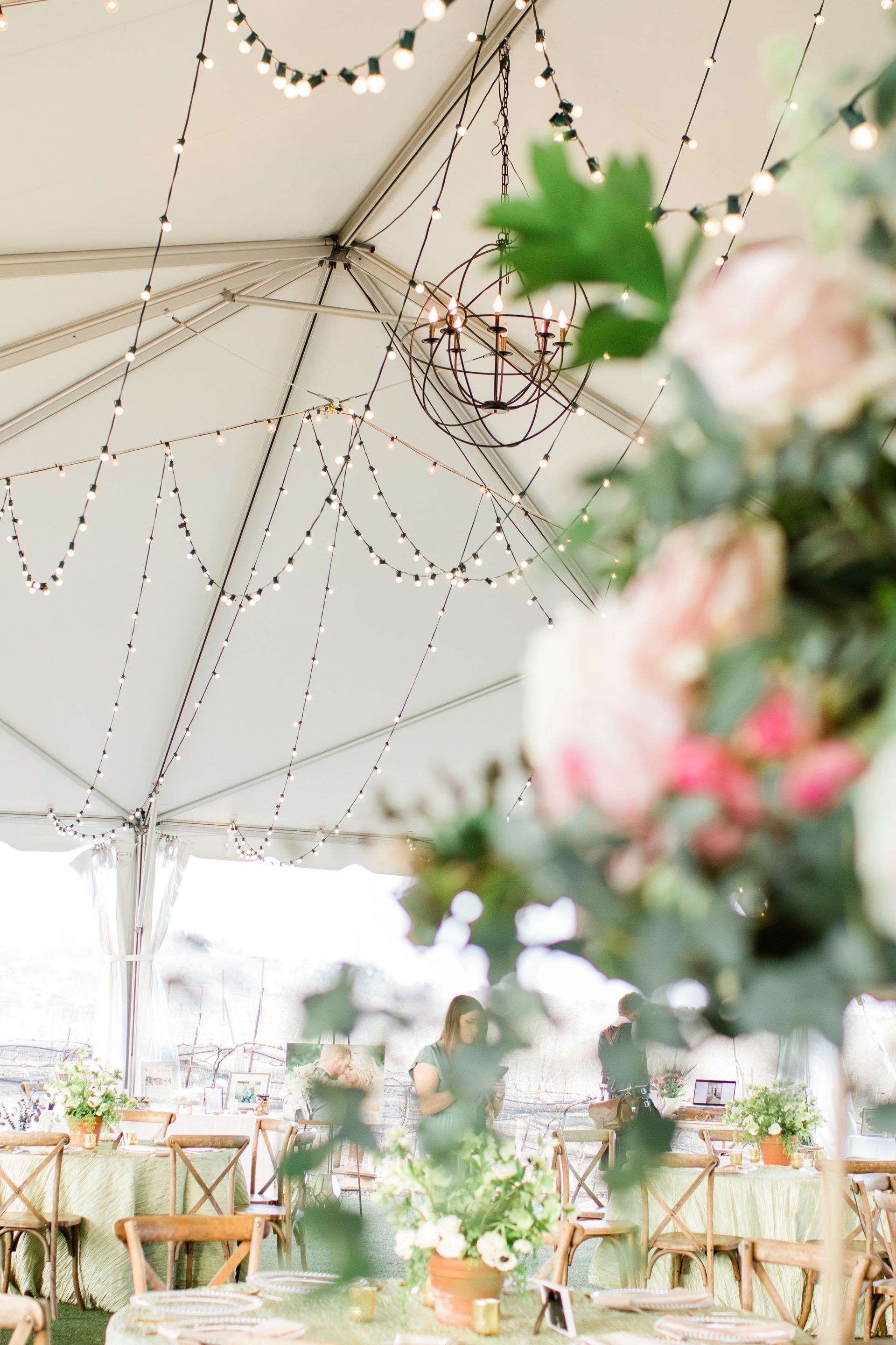 Tent with string lights, floral arrangements, and tables set for a gathering.