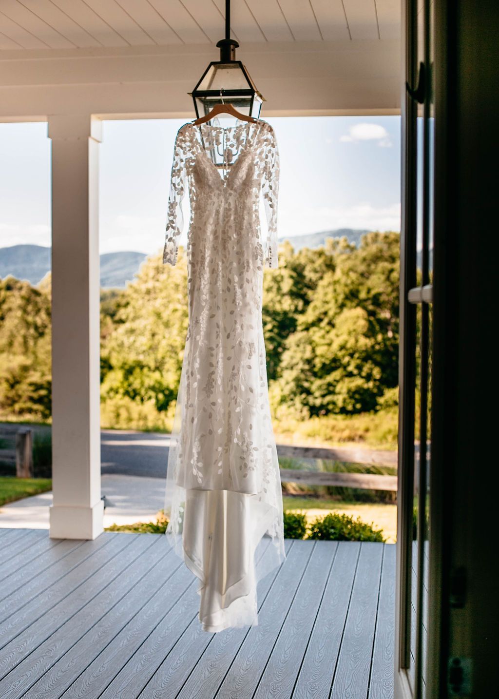 Wedding dress hanging on a wooden hanger on a porch, mountains in the background.
