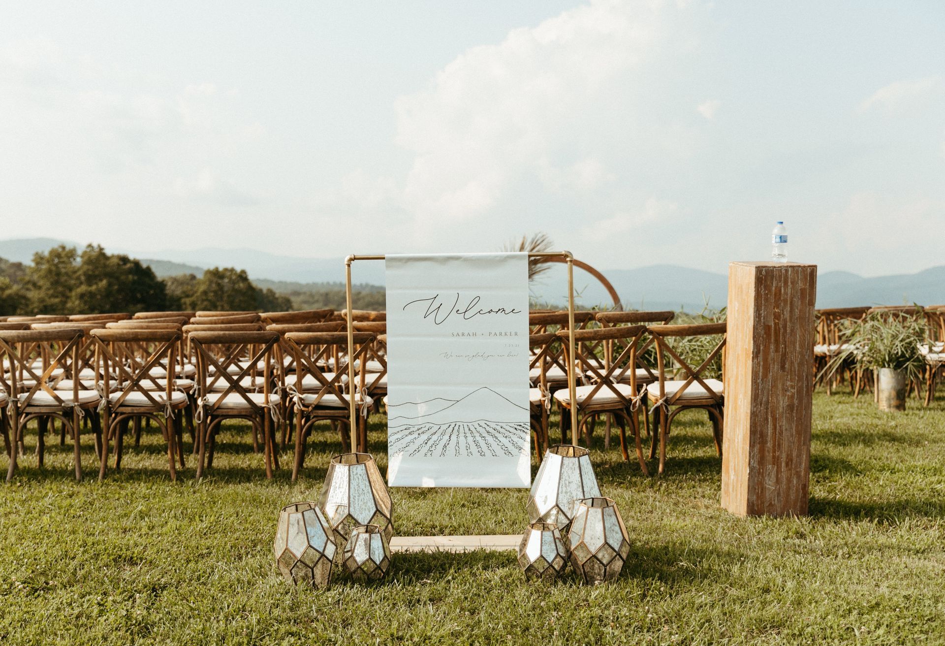 Wedding ceremony setup in field with sign, chairs, and mountainous background.