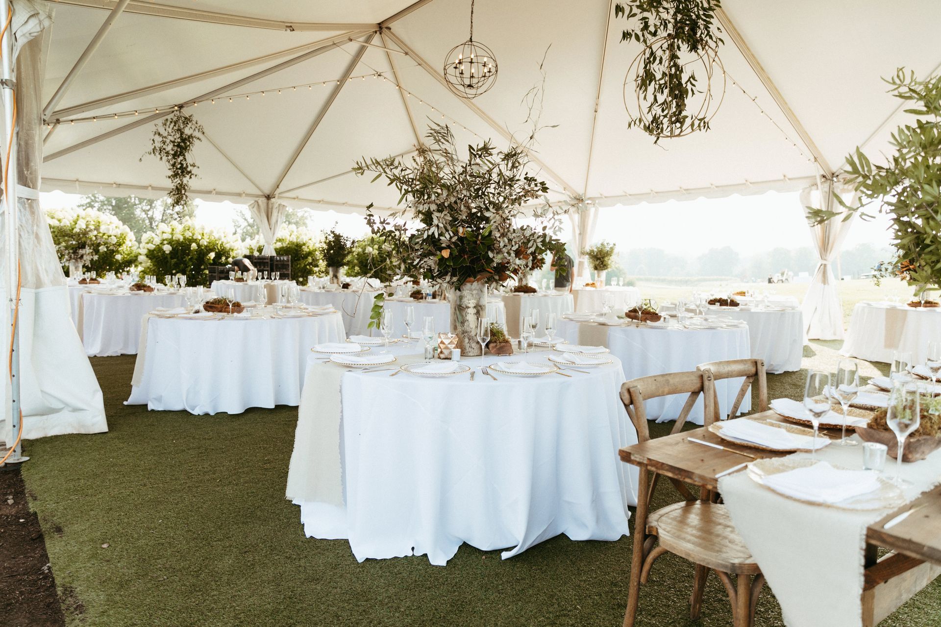 Wedding reception tent with round tables, white tablecloths, and floral centerpieces.