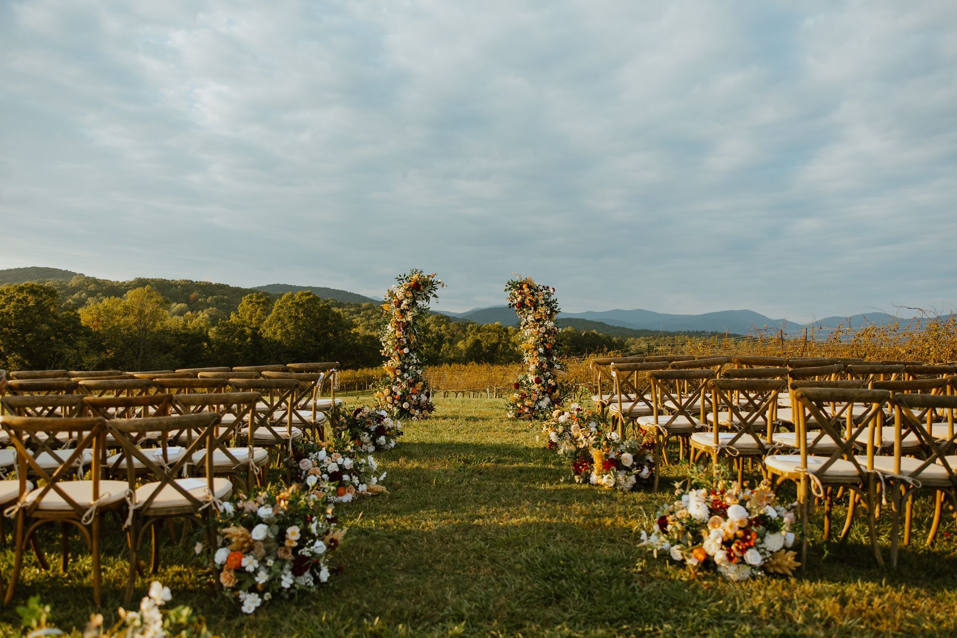 Wedding ceremony setup outdoors with floral arch, chairs, and scenic view.