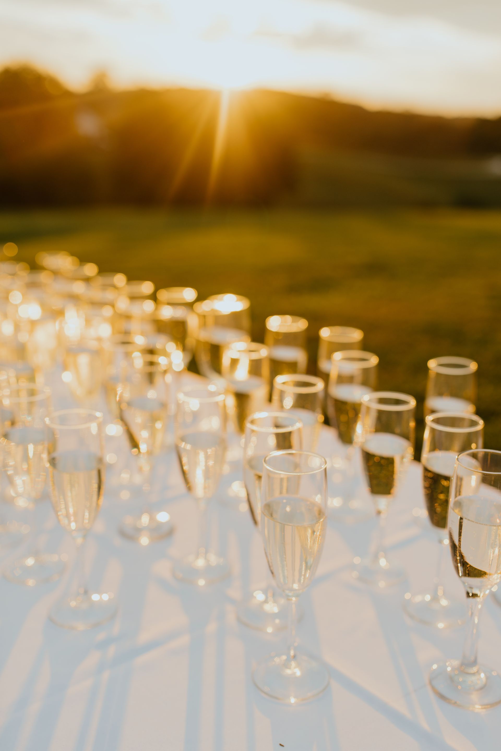 Champagne flutes filled with bubbly, arranged on a white table outdoors, backlit by a sunset.