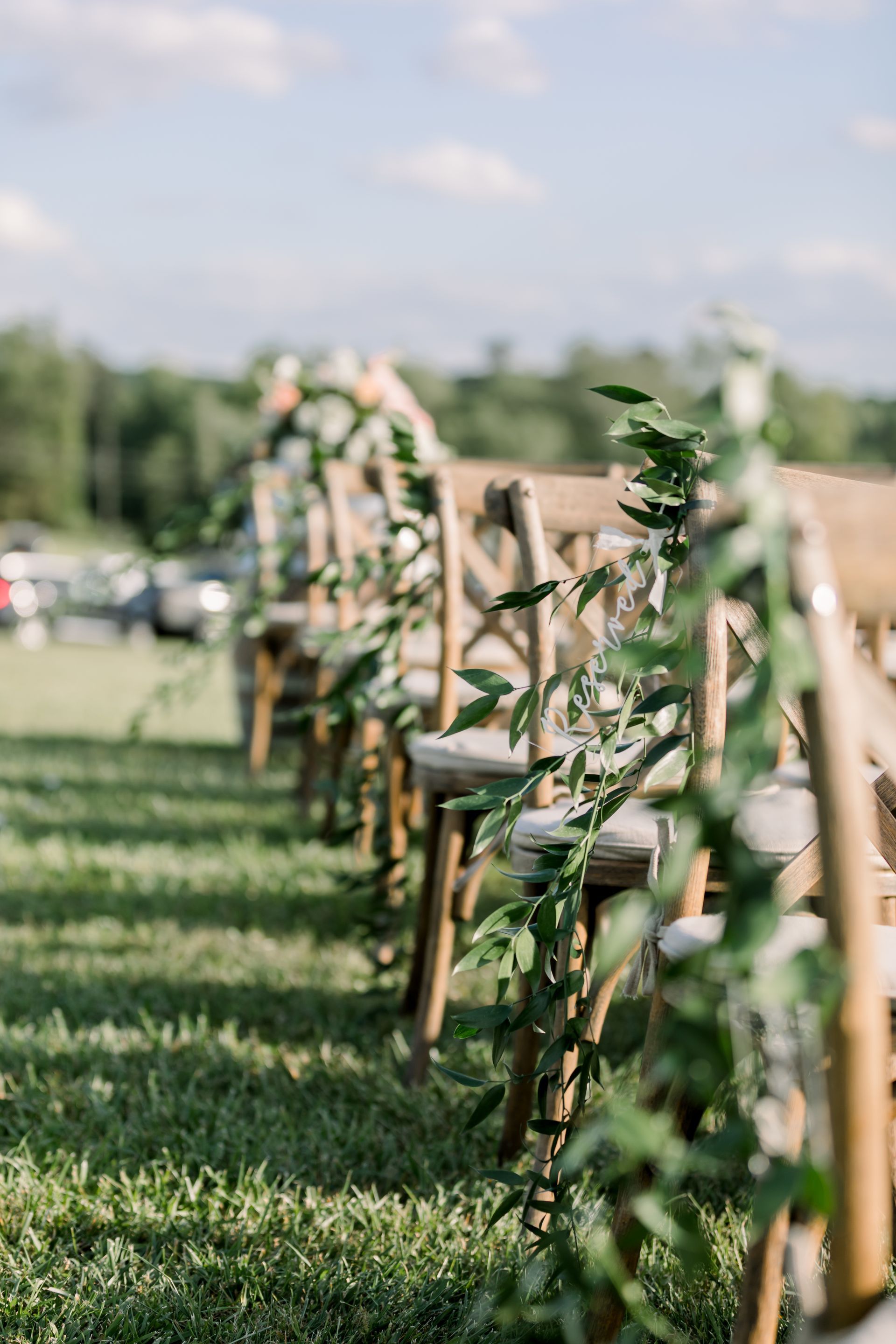 Rows of wooden chairs with greenery lining the side, set on green grass outdoors.