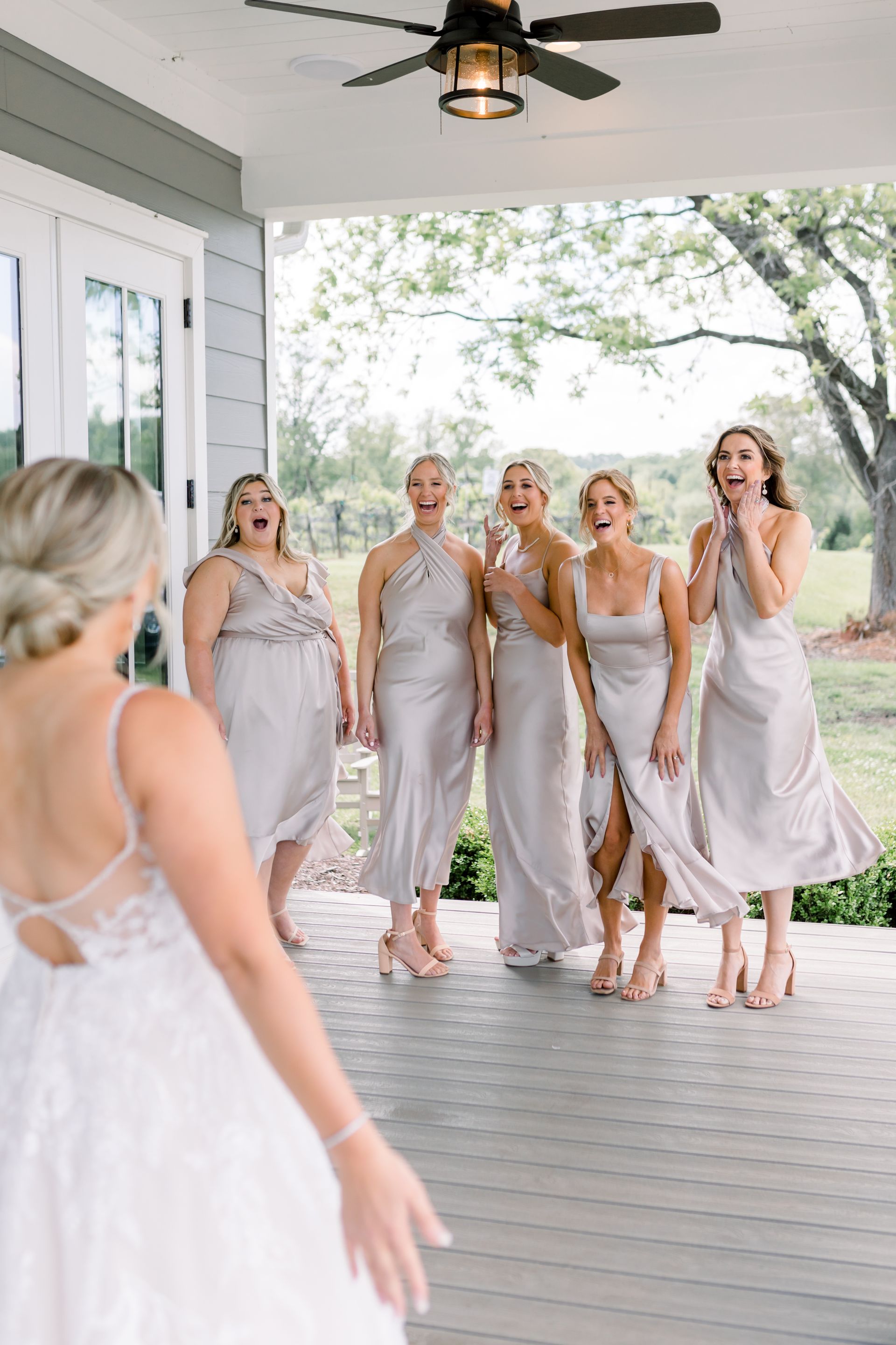 Bride in wedding dress facing five bridesmaids, who are surprised, on a porch.