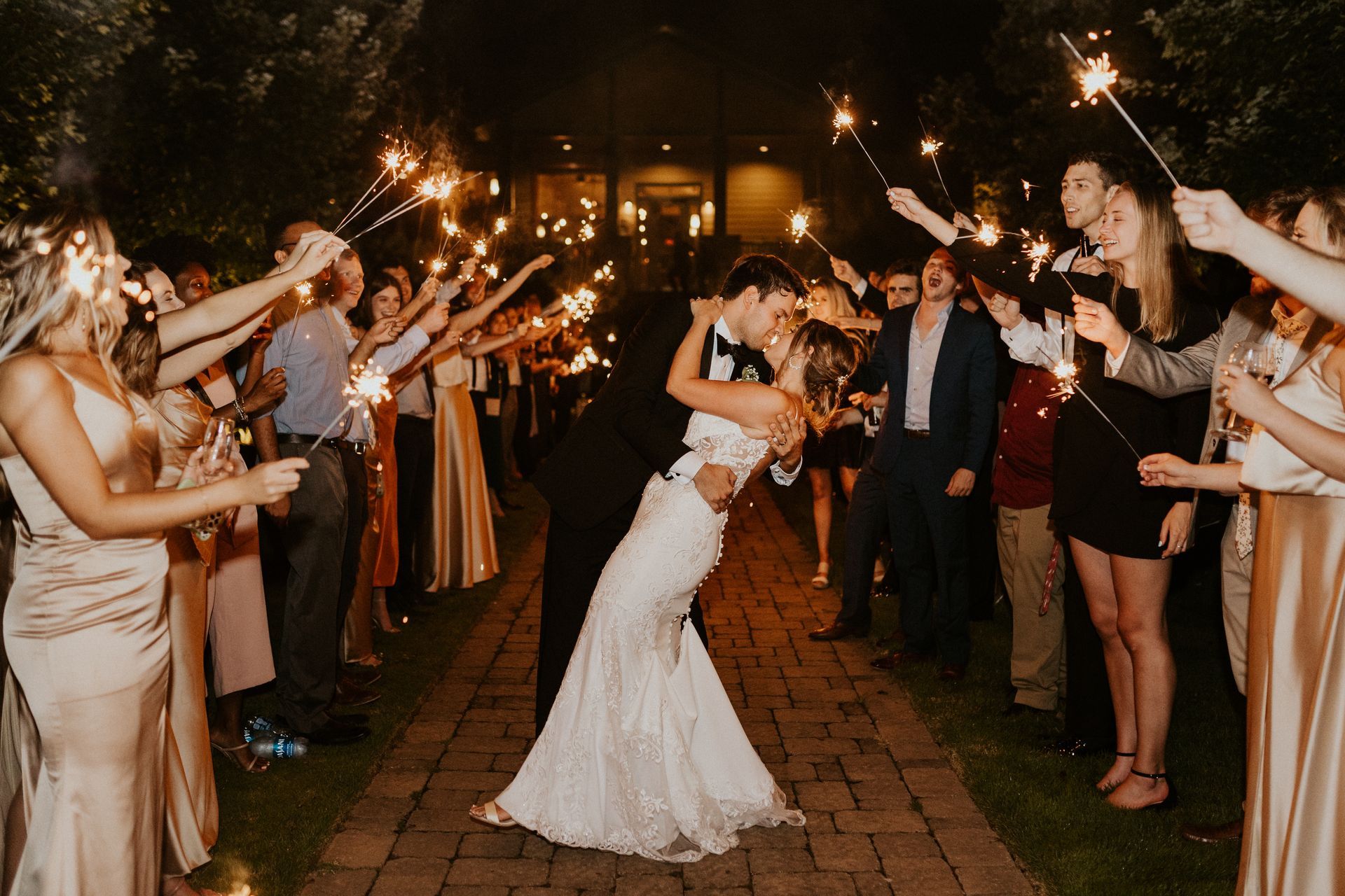 Couple kissing under sparklers held by wedding guests at night.