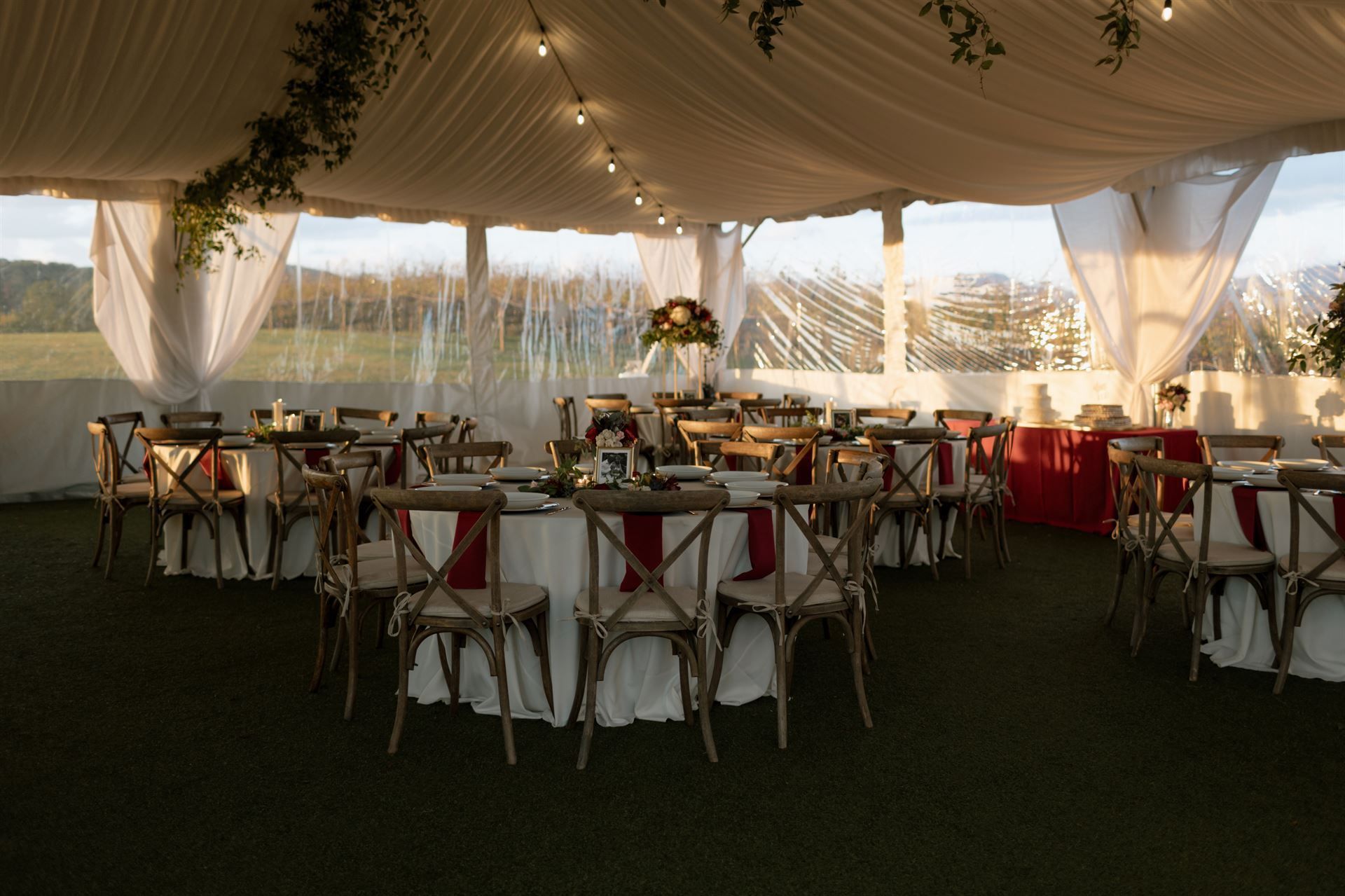 Wedding reception tent with round tables set for dining, red accents, and string lights.