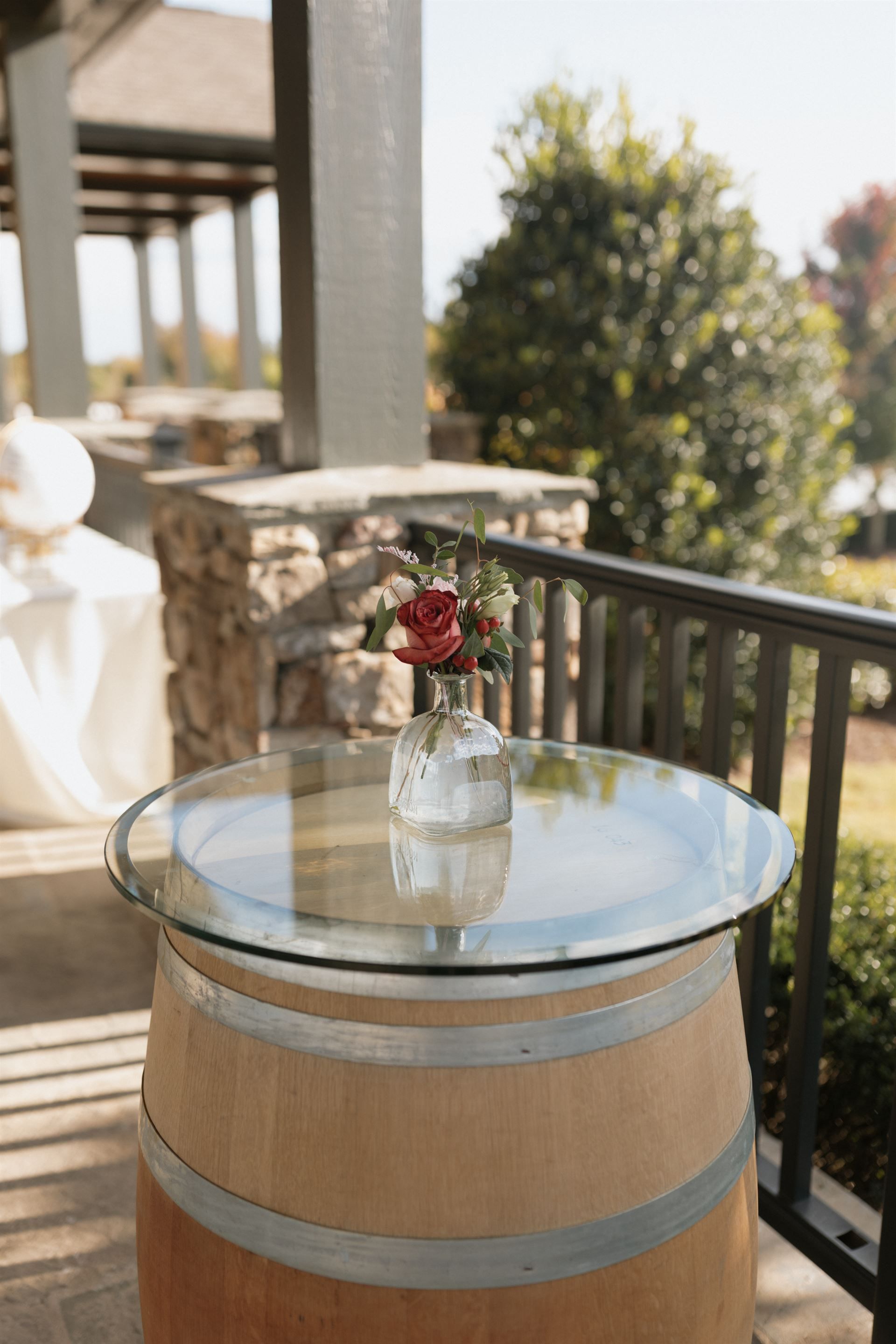 Wine barrel table with glass top and small flower arrangement outdoors.