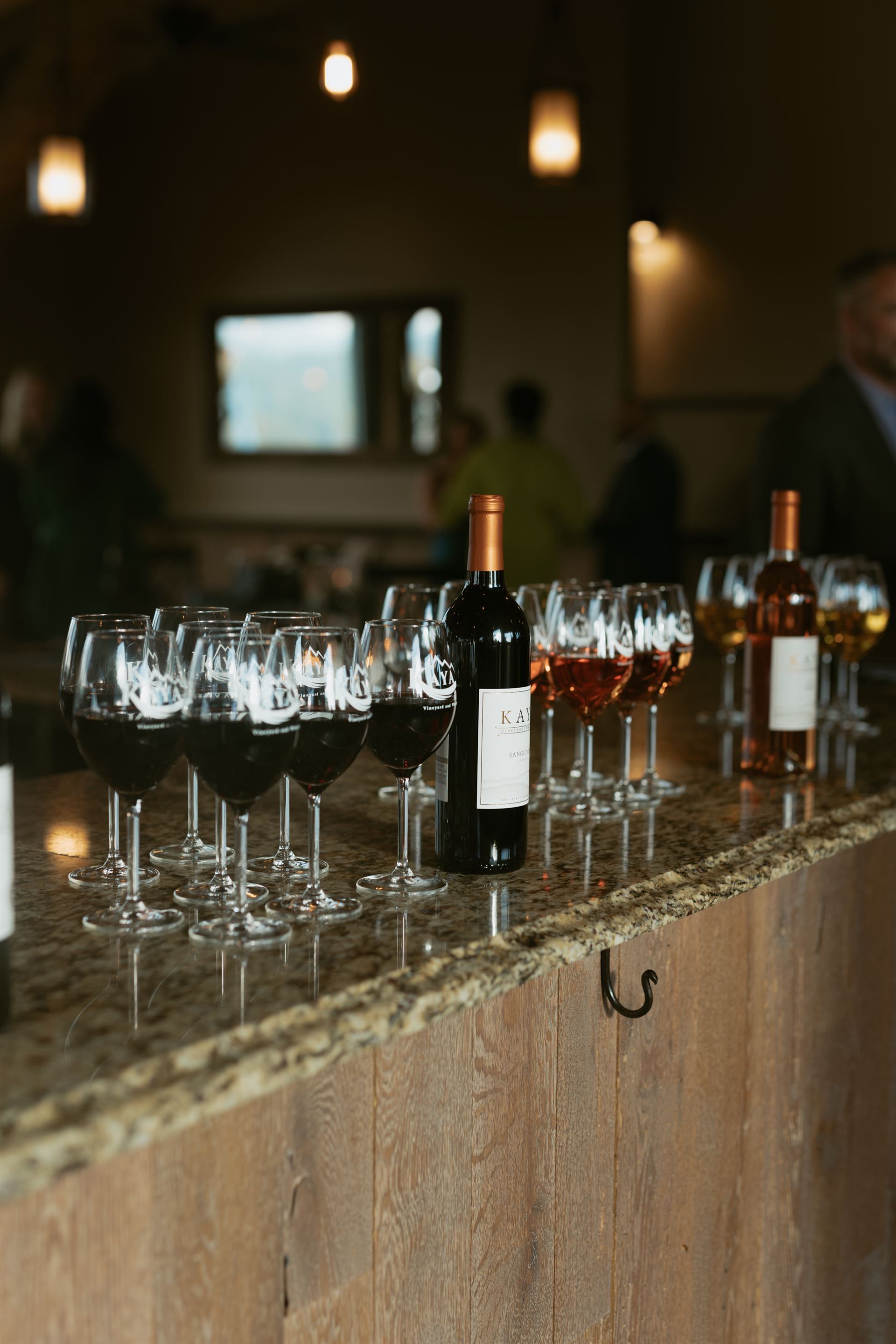 Wine bottles and glasses arranged on a bar. Dark red, rosé, and clear wine are visible.