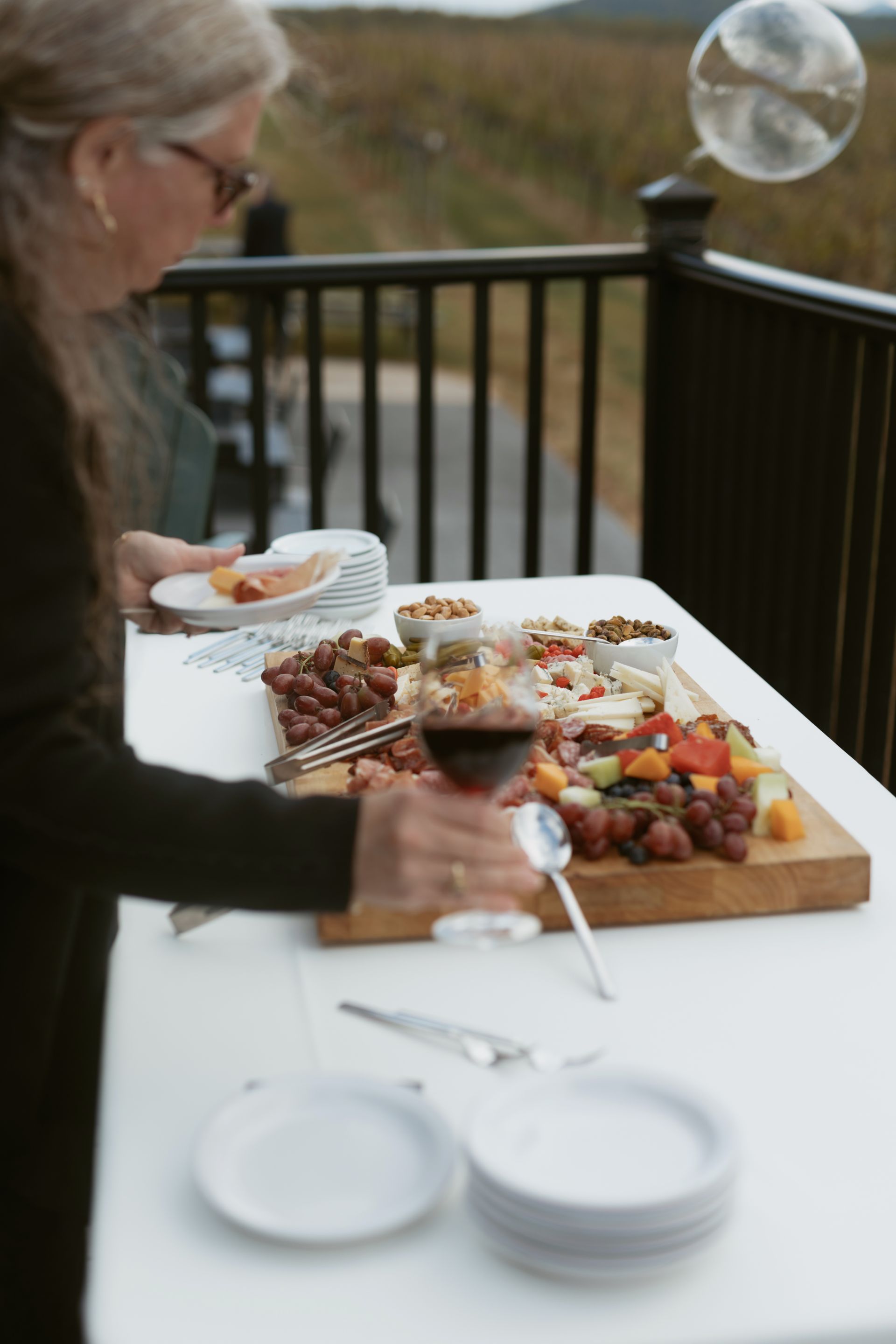 Person serving from a charcuterie board with grapes, cheese, and nuts, outdoors on a deck.
