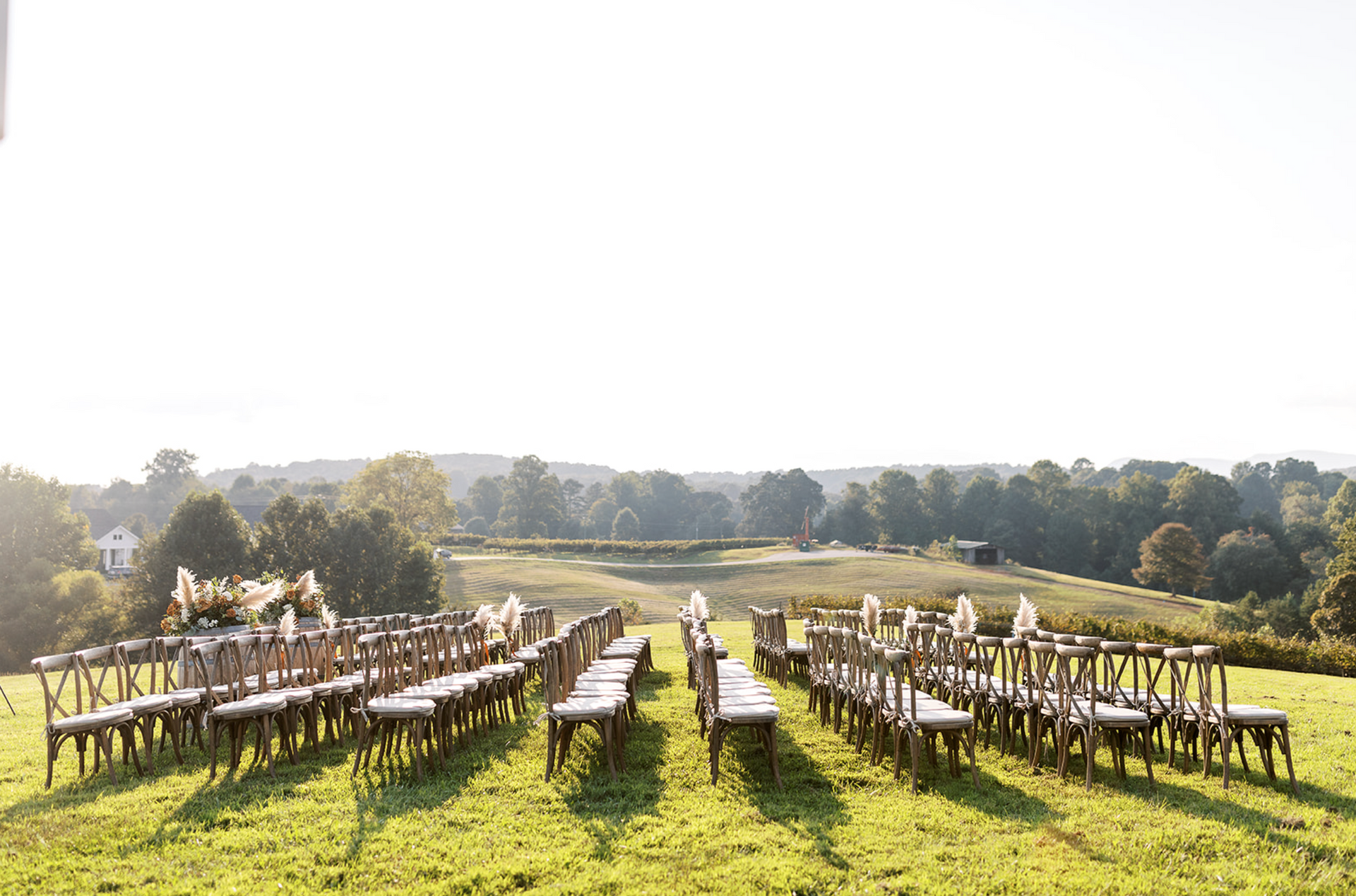 Outdoor wedding ceremony seating in a grassy field with a scenic countryside view.