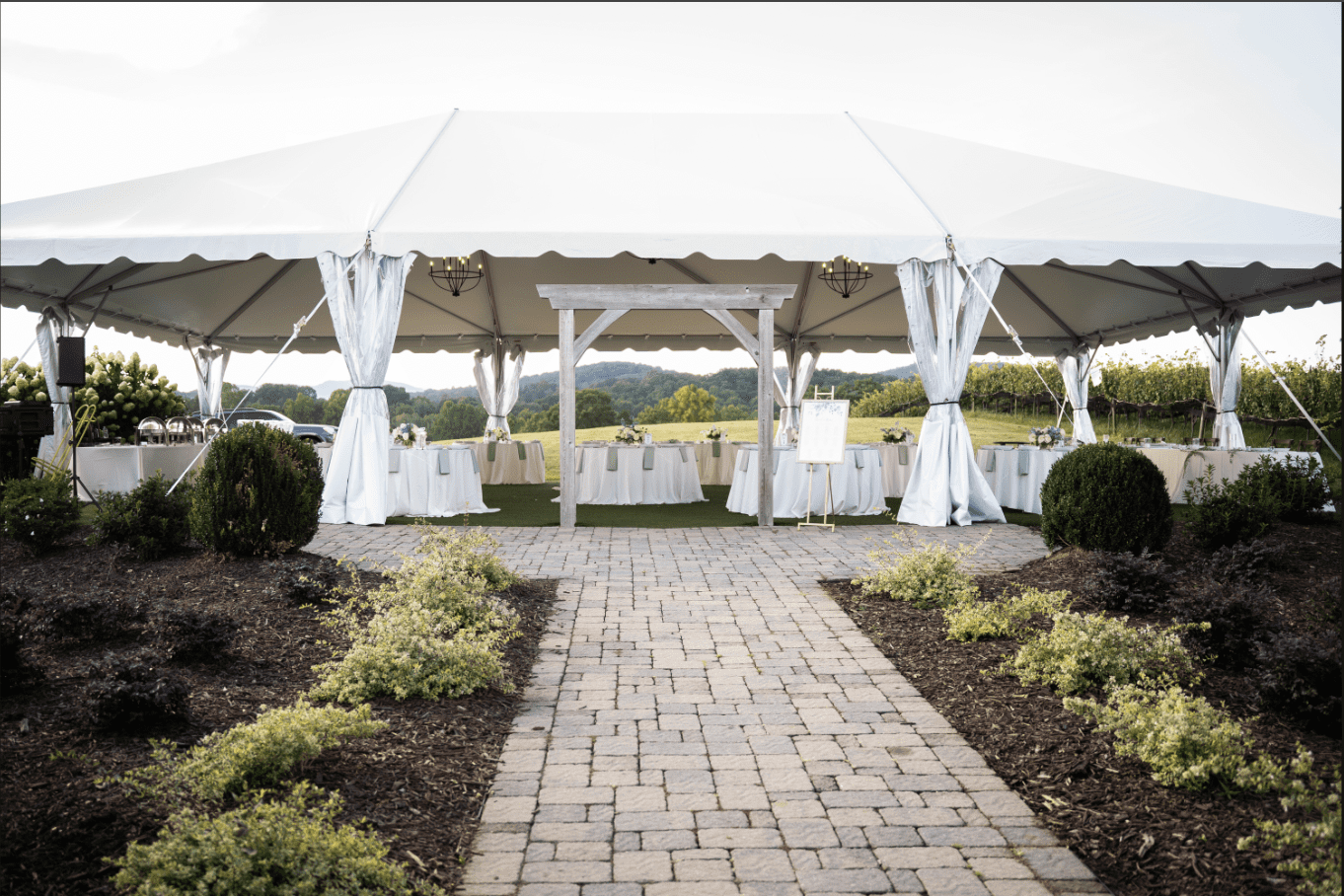 Wedding tent on a brick path, tables set for guests, outdoor setting with a view.