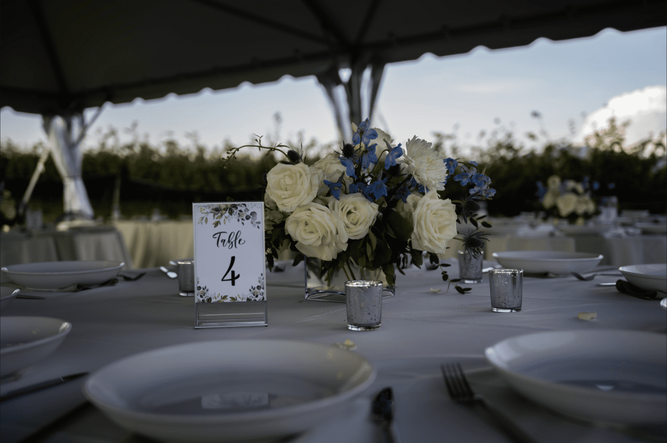 Table setting with floral centerpiece and table number under a tent.