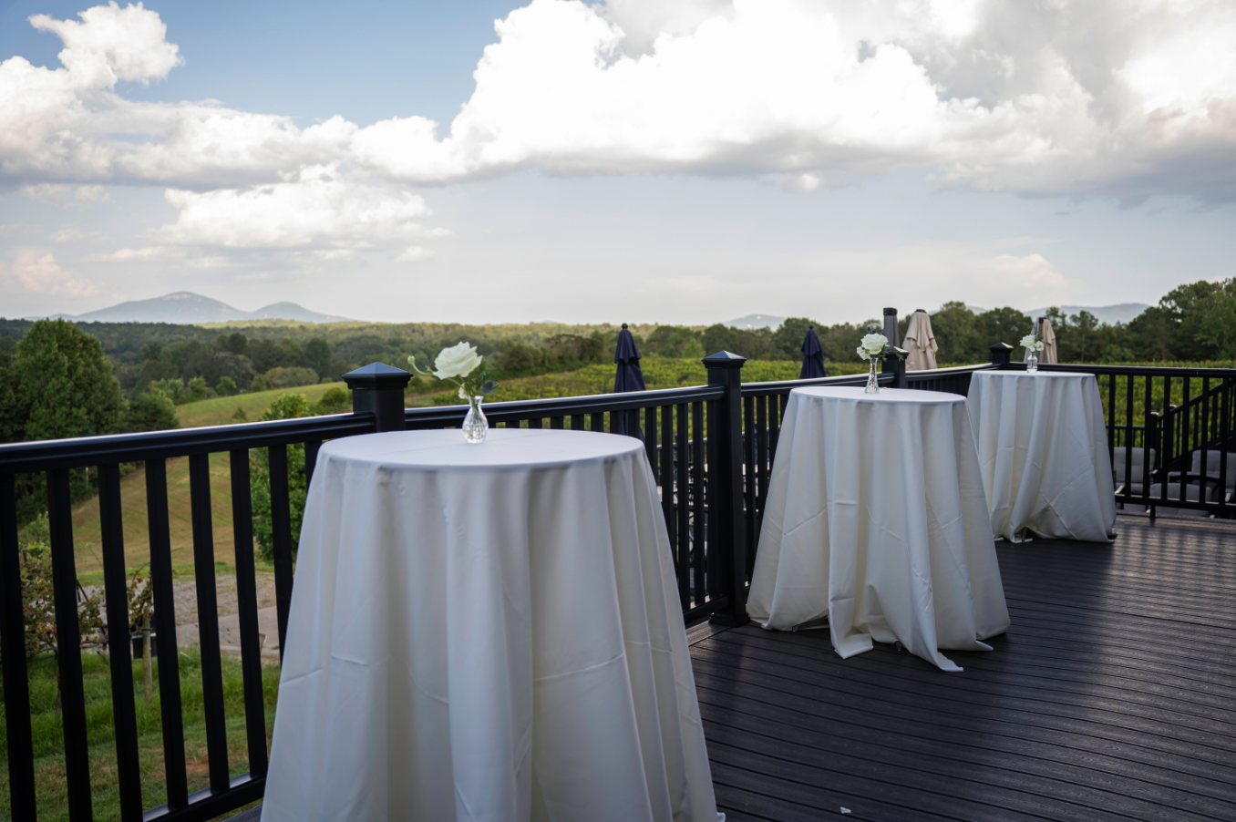 Outdoor deck with white-covered tables, overlooking a scenic valley under a cloudy sky.
