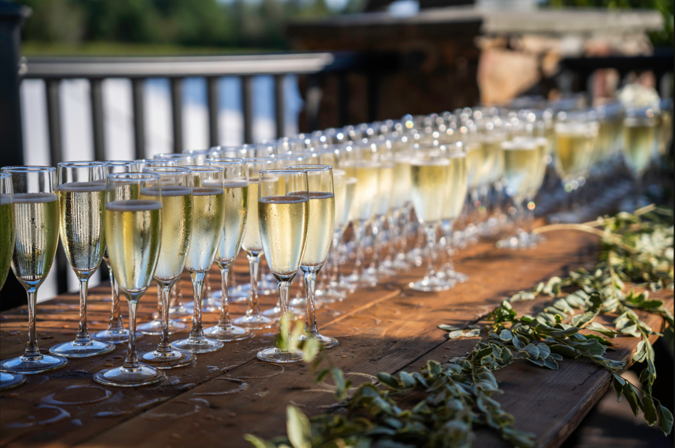 Rows of champagne flutes on a rustic wooden table, likely for a celebration.