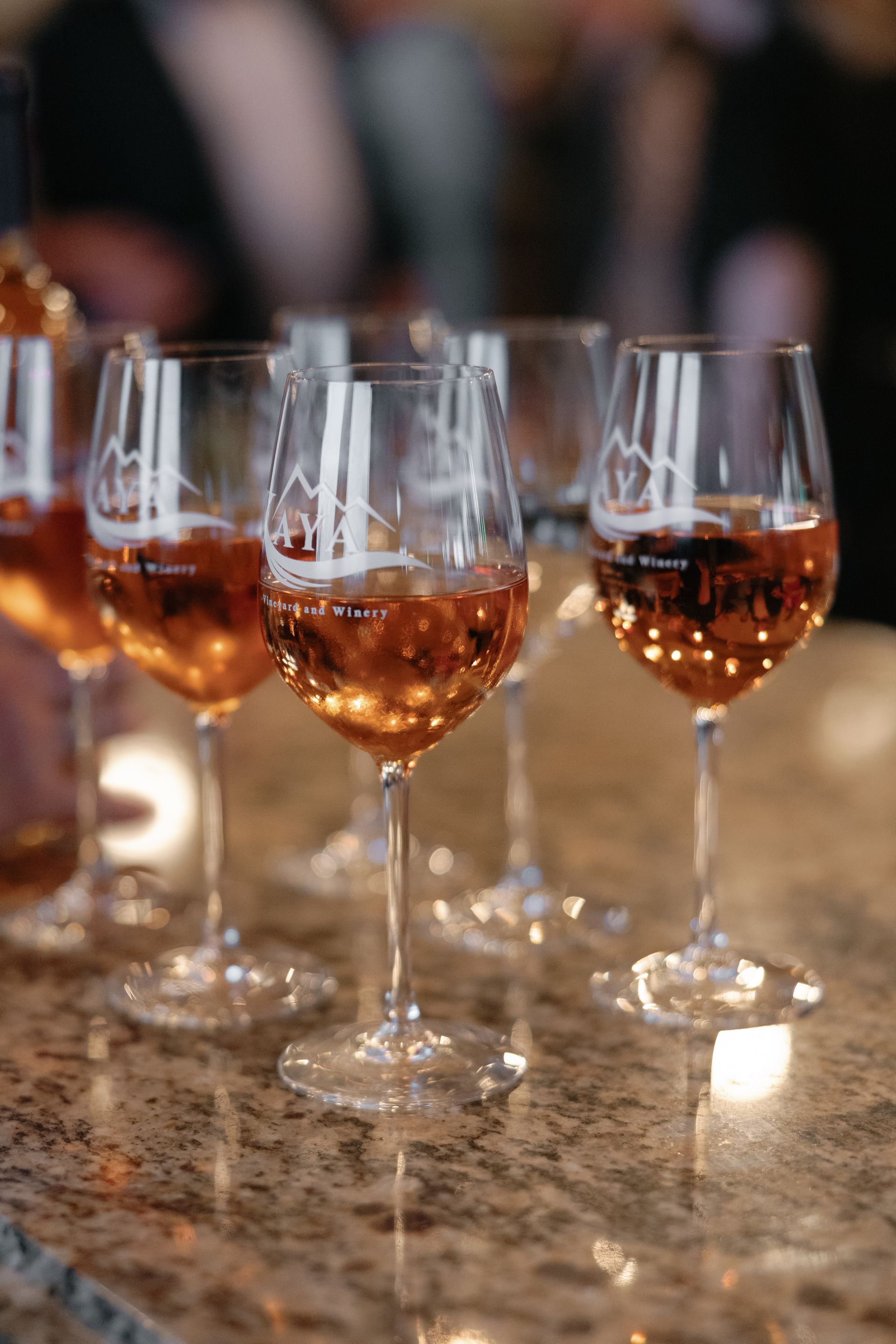 Wine glasses filled with amber liquid on a countertop, soft lighting.
