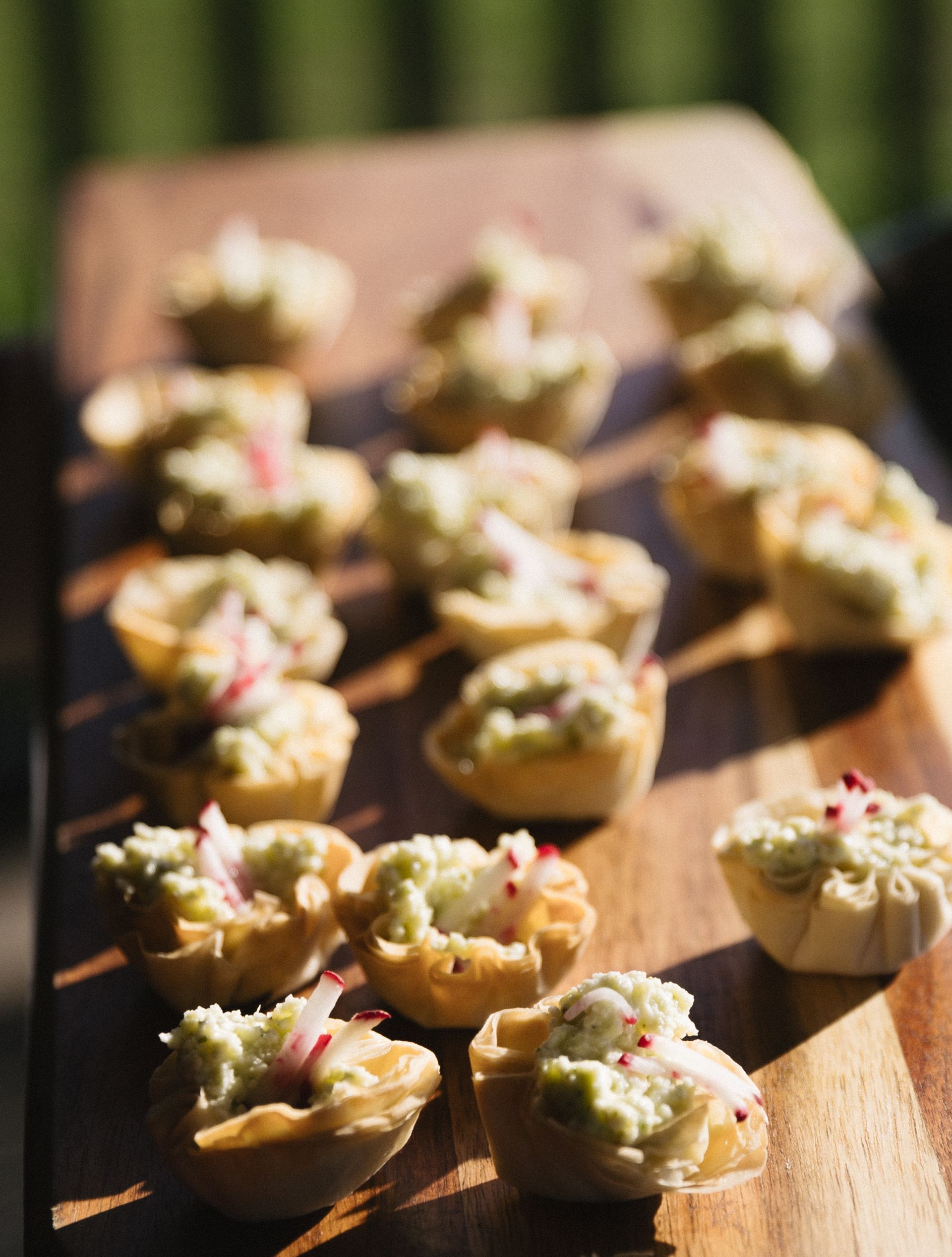 Miniature quiche bites with green filling, topped with radish on a wooden board.