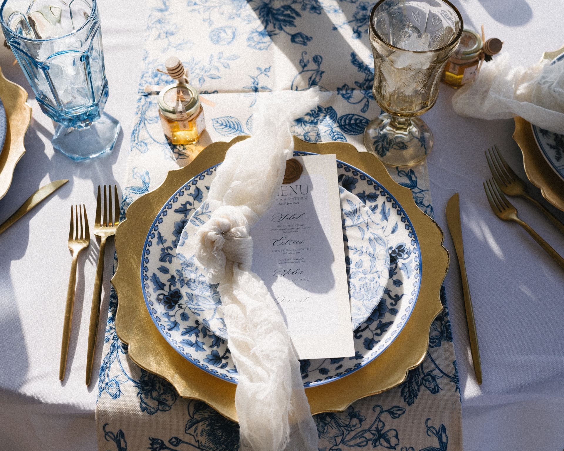 Elegant table setting with gold chargers, blue and white plates, and gold flatware.