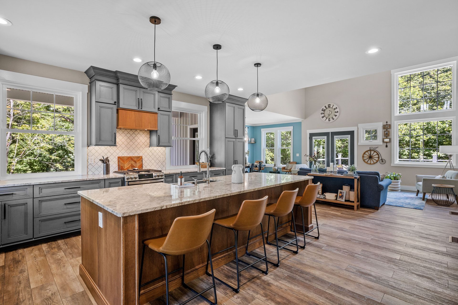 Modern kitchen with a granite island, leather bar stools, dark cabinets, and an open floor plan leading to a living area.