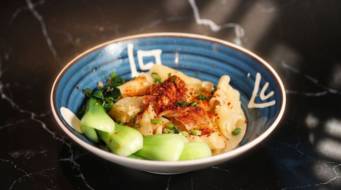 Blue bowl of rice with sliced cucumber and grilled chicken on a dark table