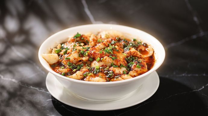 Bowl of spicy soup topped with herbs and sesame seeds on a dark table