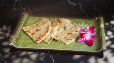 Grilled flatbread slices on a green plate with a pink orchid garnish on a dark marble surface