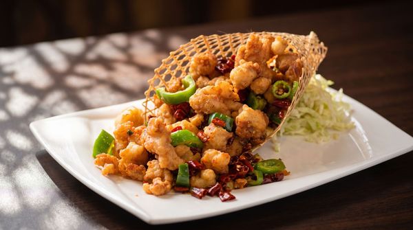 Crispy fried chicken topped with scallions and sauce on a white plate with shredded cabbage
